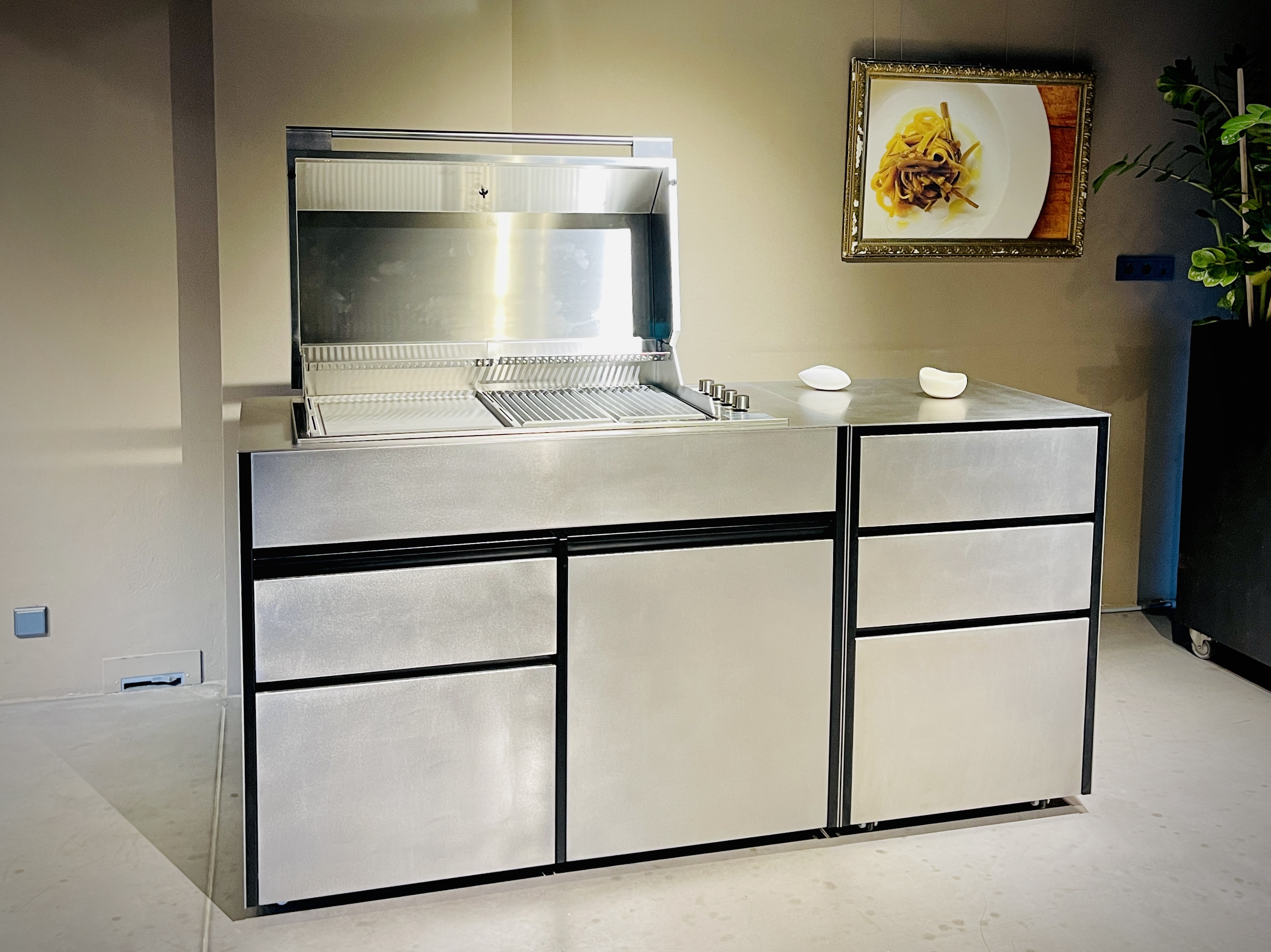 Outdoor-Küche mit geschlossenem Edelstahlkorpus und geöffnetem Grilldeckel