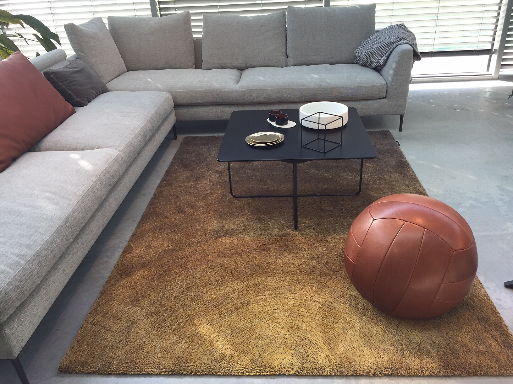 Rechteckiger Teppich in Braun zwischen grauem Sofa, Lederball und Couchtisch