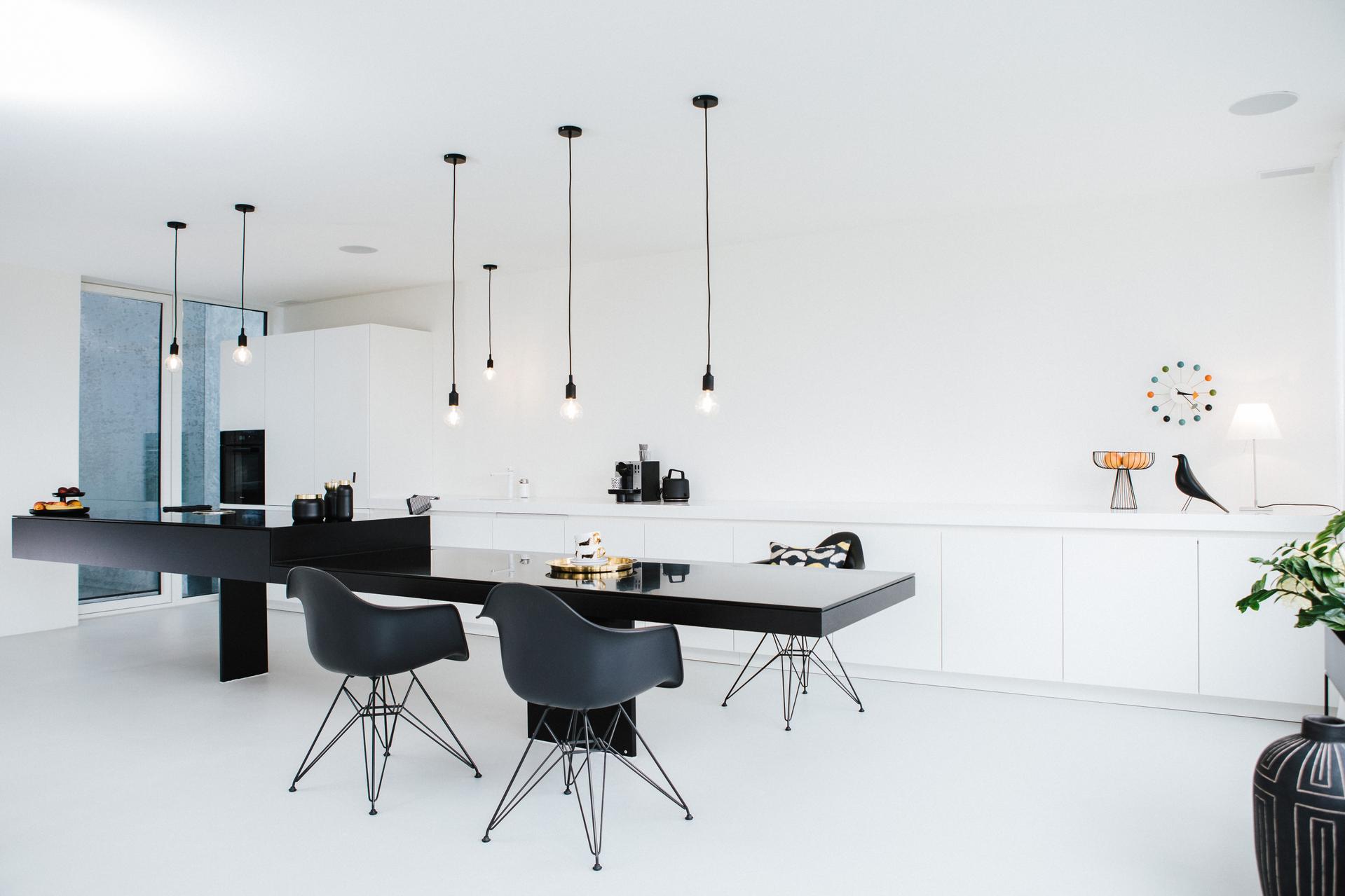 Minimalistische Küche mit weißen Fronten und markanter schwarzer Theke und passenden Armlehnsesseln.