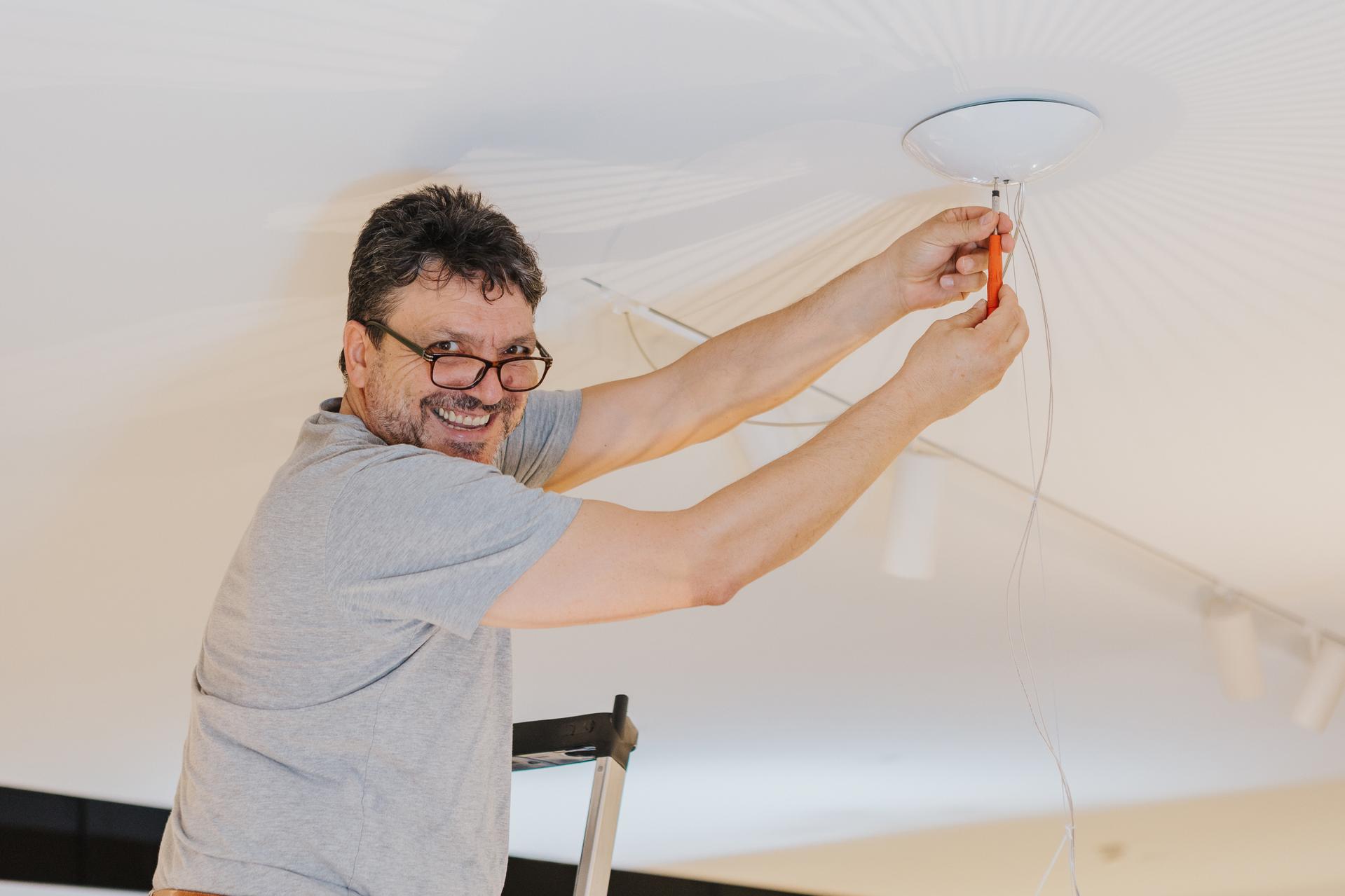 Ein Mitarbeiter von Seipp Wohnen montiert gut gelaunt eine Leuchte an einer weißen Decke  