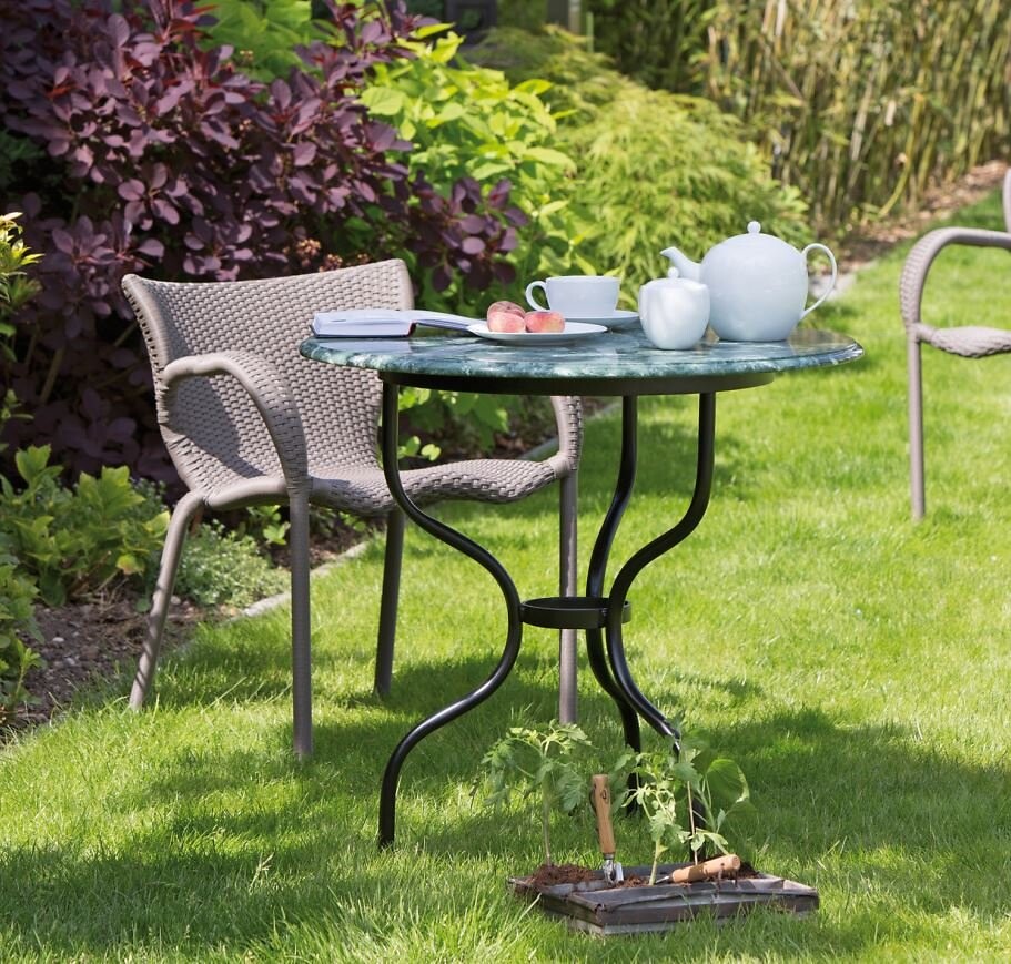 Gartenszene mit rundem Tisch aus Metall und Teeservice auf grünem Rasen  