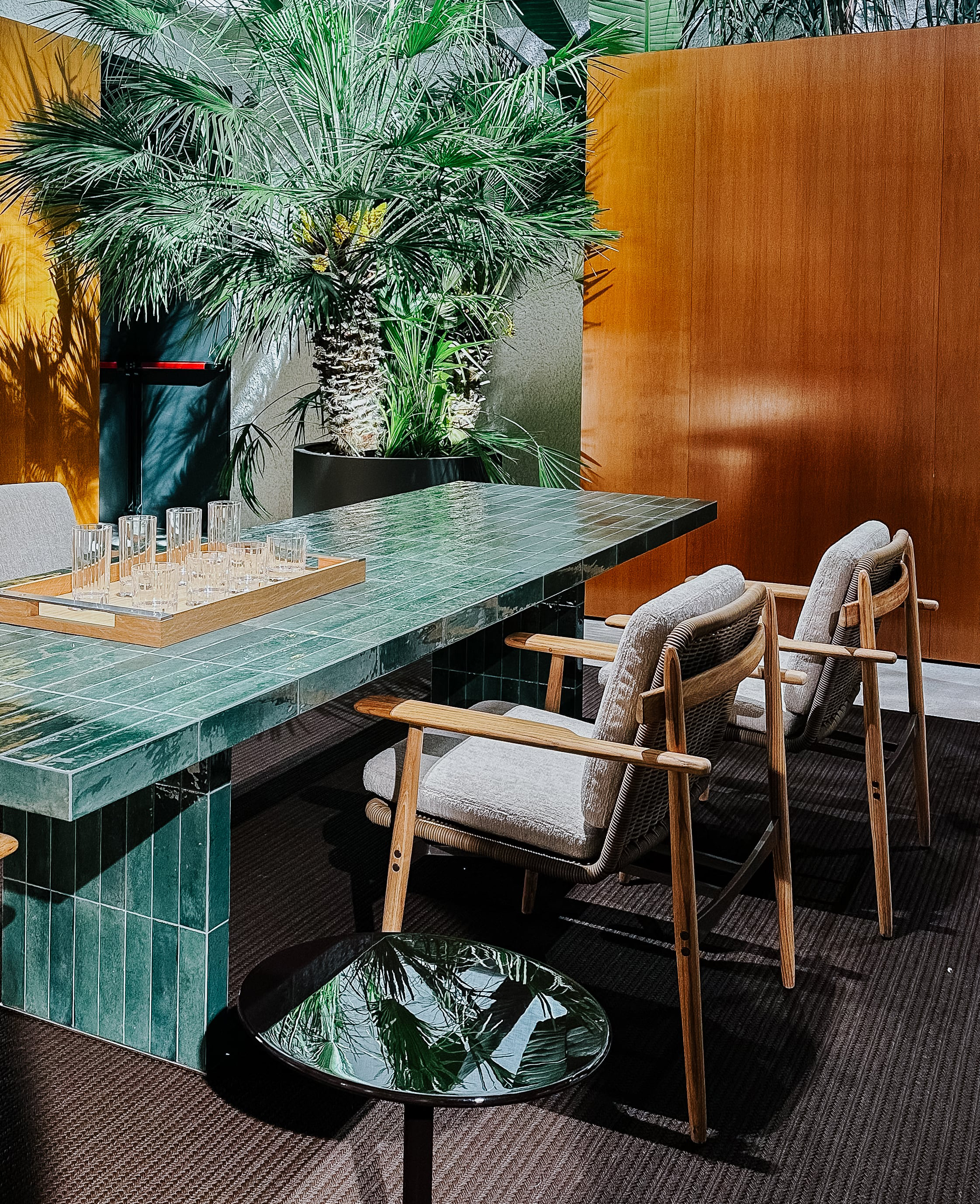 Andrée Dining Outdoor Tisch von Minotti, vollständig mit grüner, glasierter Keramik verkleidet. Die strenge Geometrie und der Bezug zu den 70er-Jahren stehen im Kontrast zur üppigen Begrünung im Hintergrund.