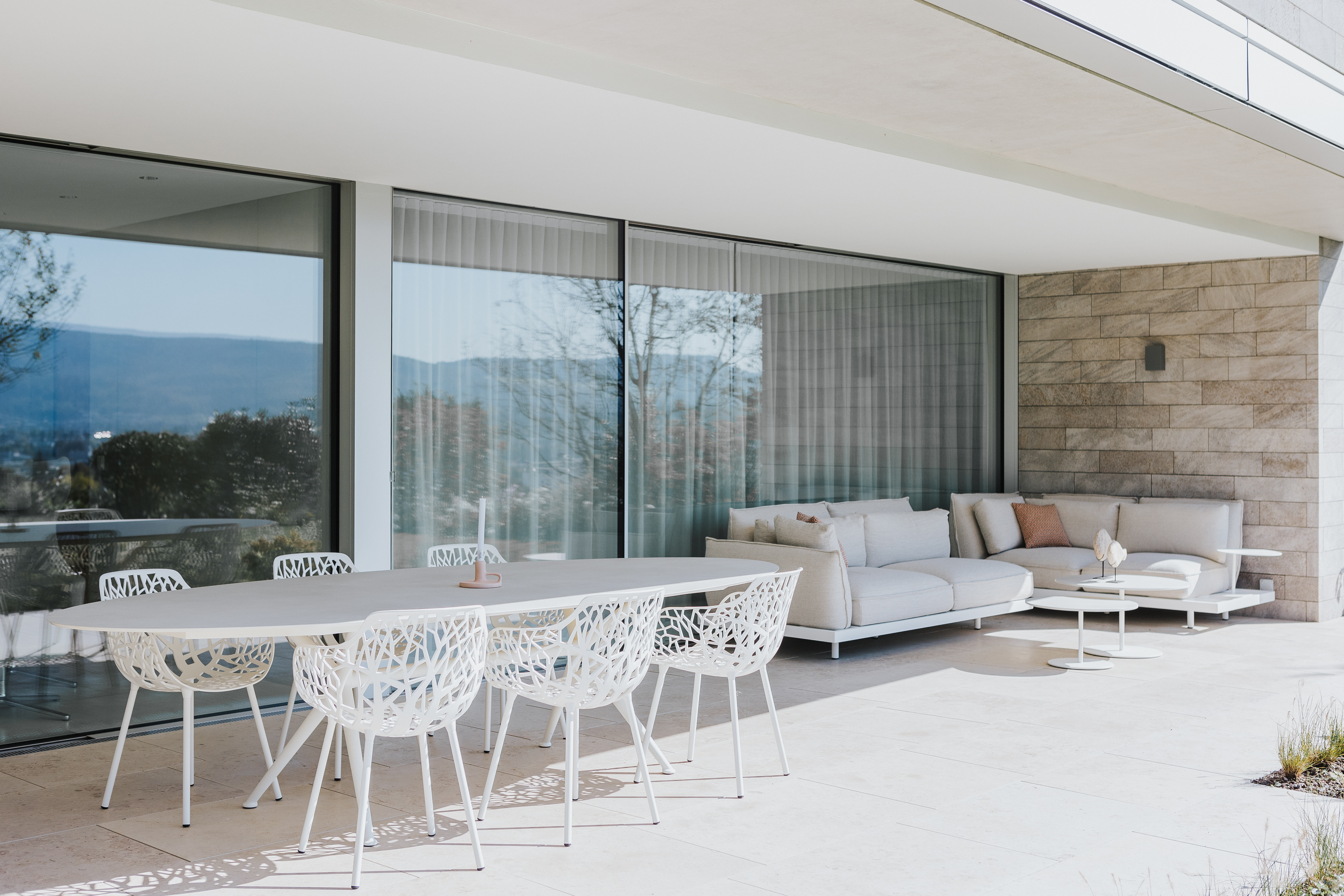 Überdachte Terrasse mit filigranem Outdoor-Essbereich und Lounge-Sofa in ruhiger, grüner Hanglage.