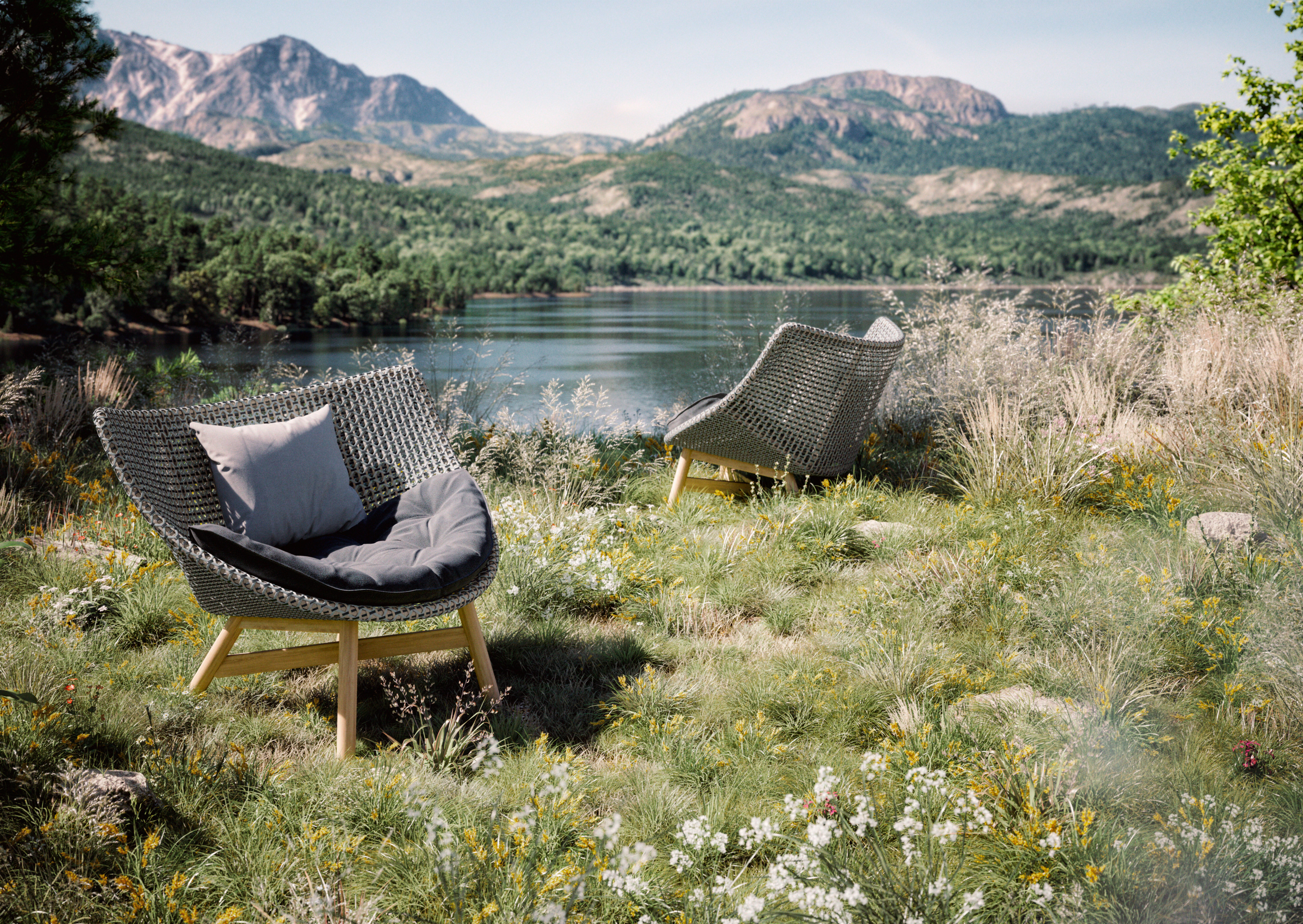 Zwei geflochtene Loungesessel mit grauen Polstern in natürlicher Landschaft an einem Seeufer platziert
