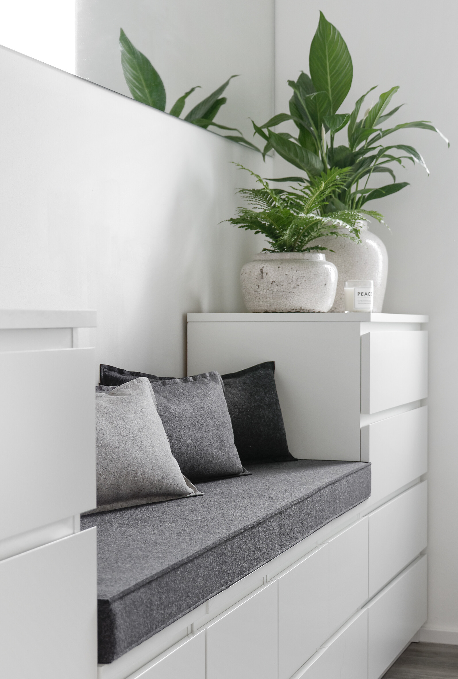Graues Filzpolster auf weißer Stauraumbank mit Pflanzen und Kissen im Flur