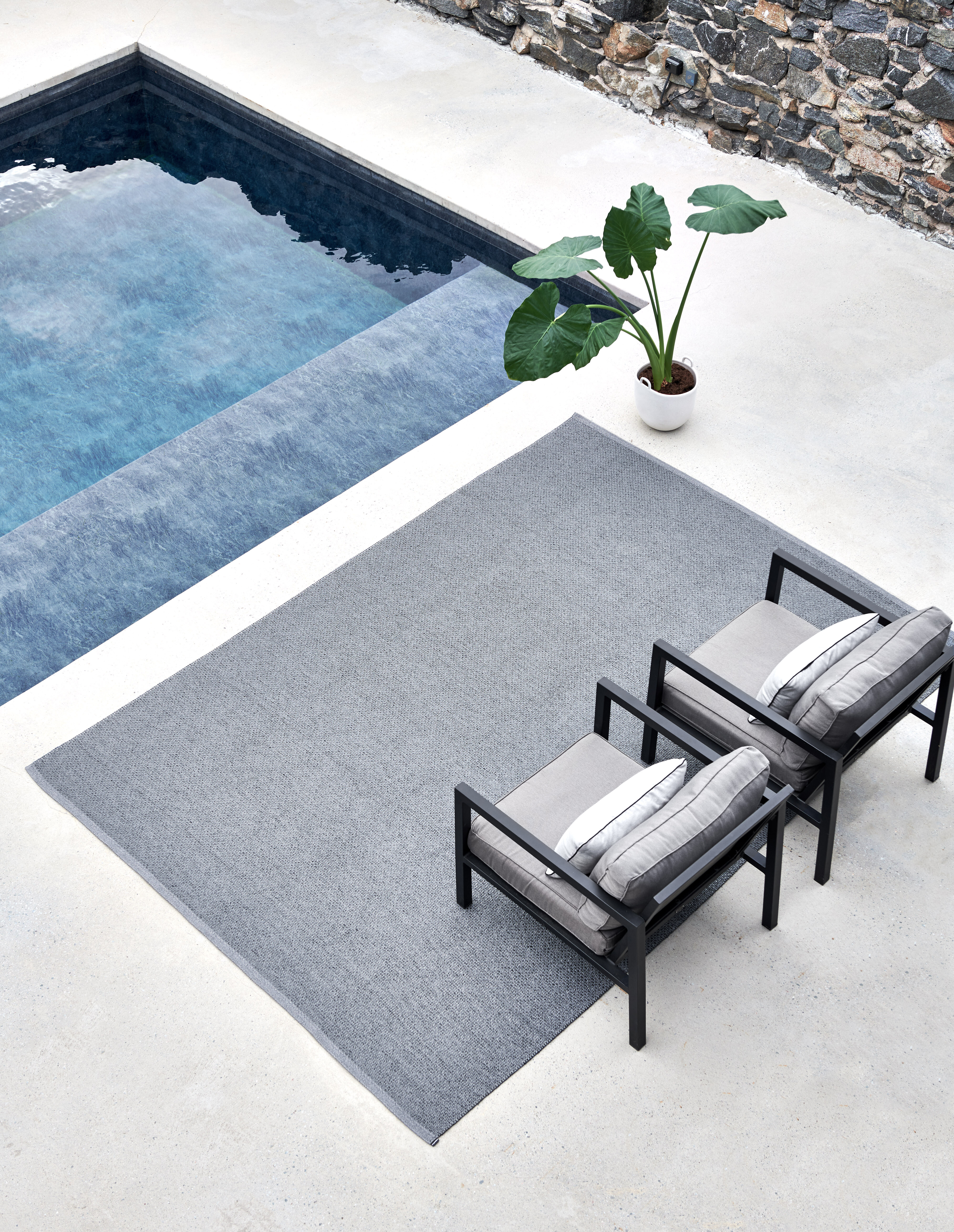Zwei Loungesessel auf grauem Outdoorteppich neben einem Pool mit dunklen Fliesen  