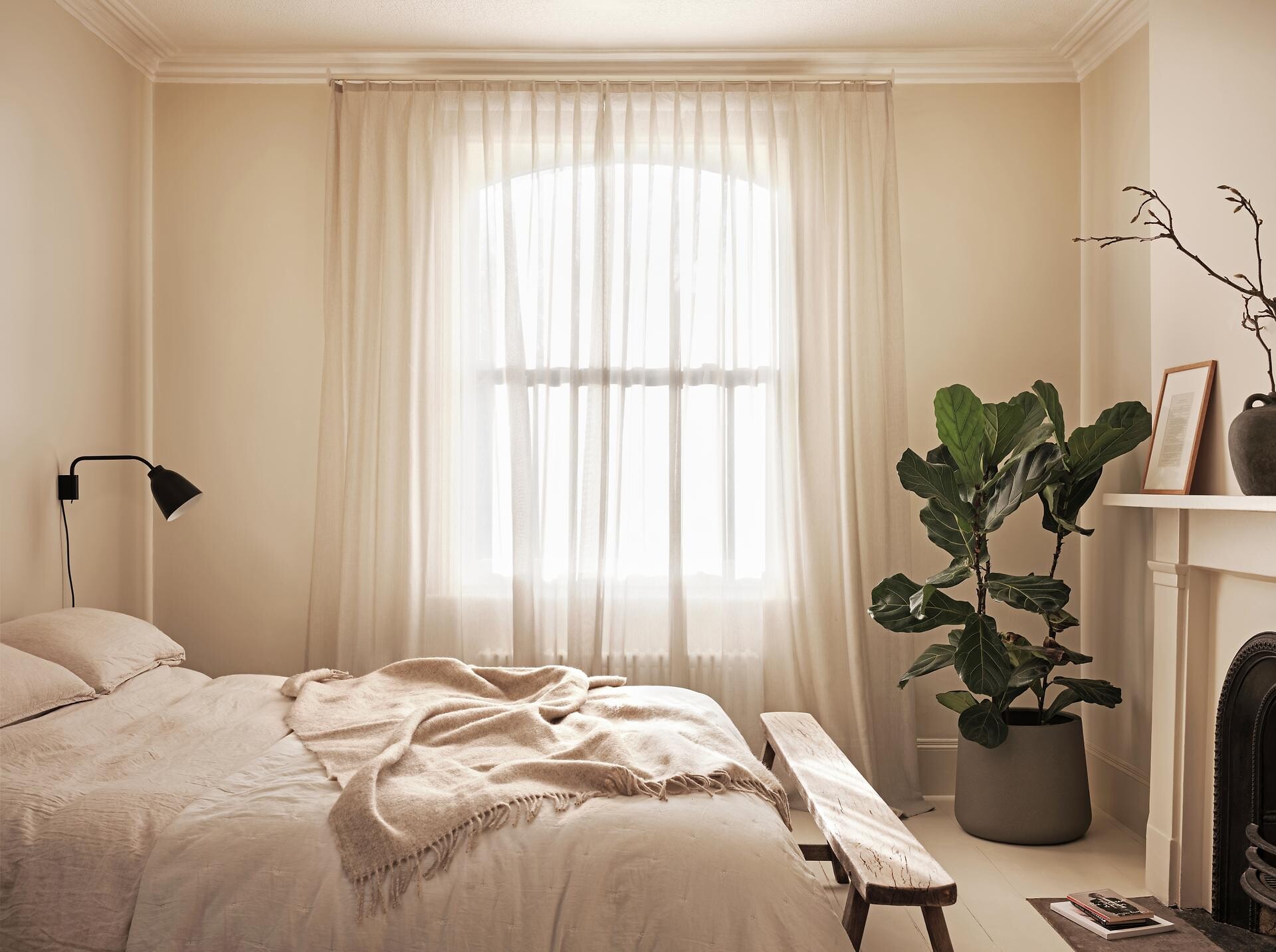 Lichtdurchlässiger Vorhang in einem hellen Schlafzimmer mit Bett und Pflanze