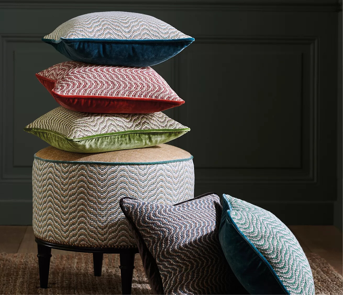 Gestapelte Kissen mit grafischen Mustern in kräftigen Farben auf Hocker aus gleichem Stoff