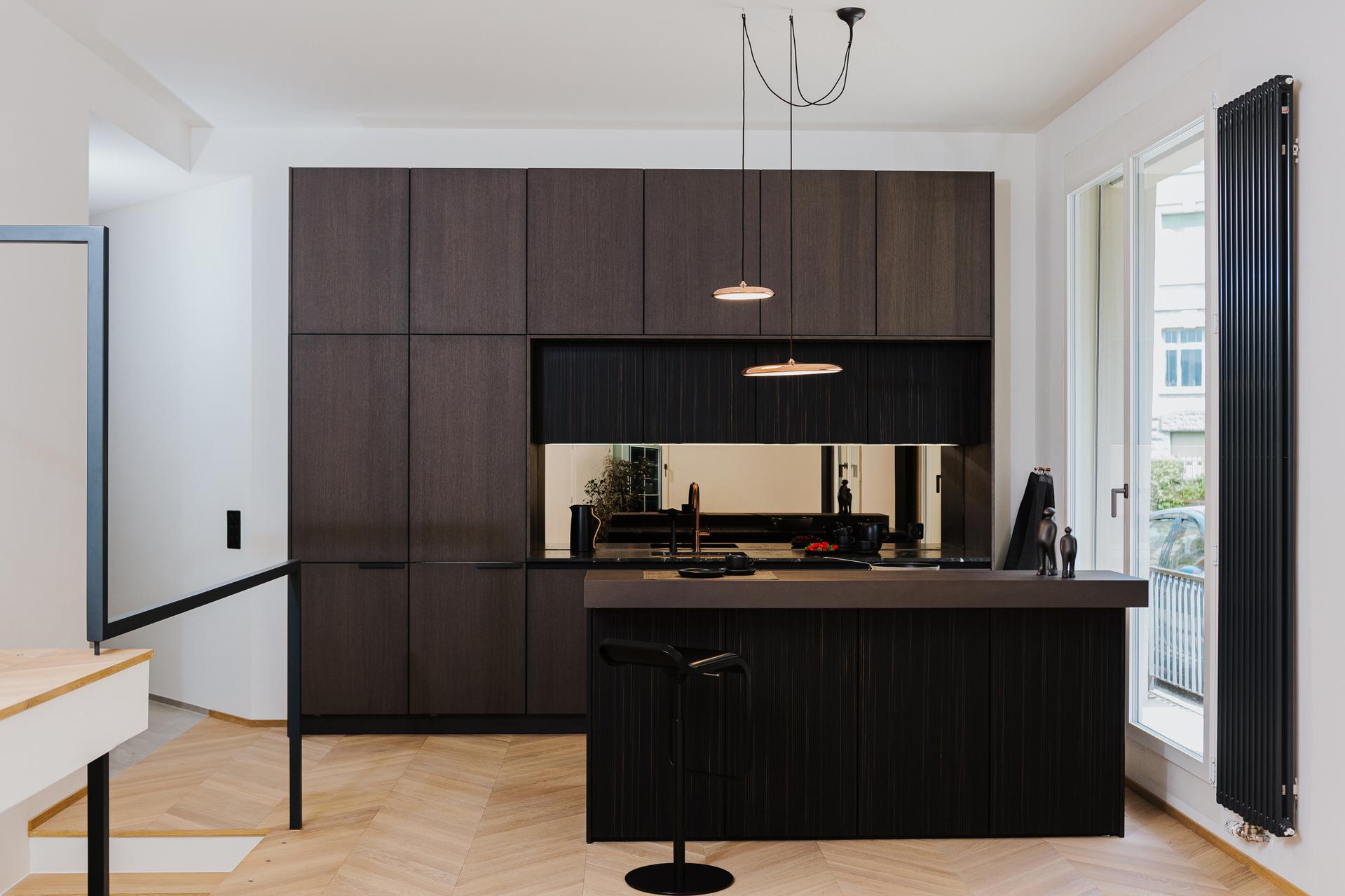 Dunkle SieMatic Küche mit vertikal strukturierter Holzfront, Spiegelscheibe und Naturstein-Arbeitsfläche.