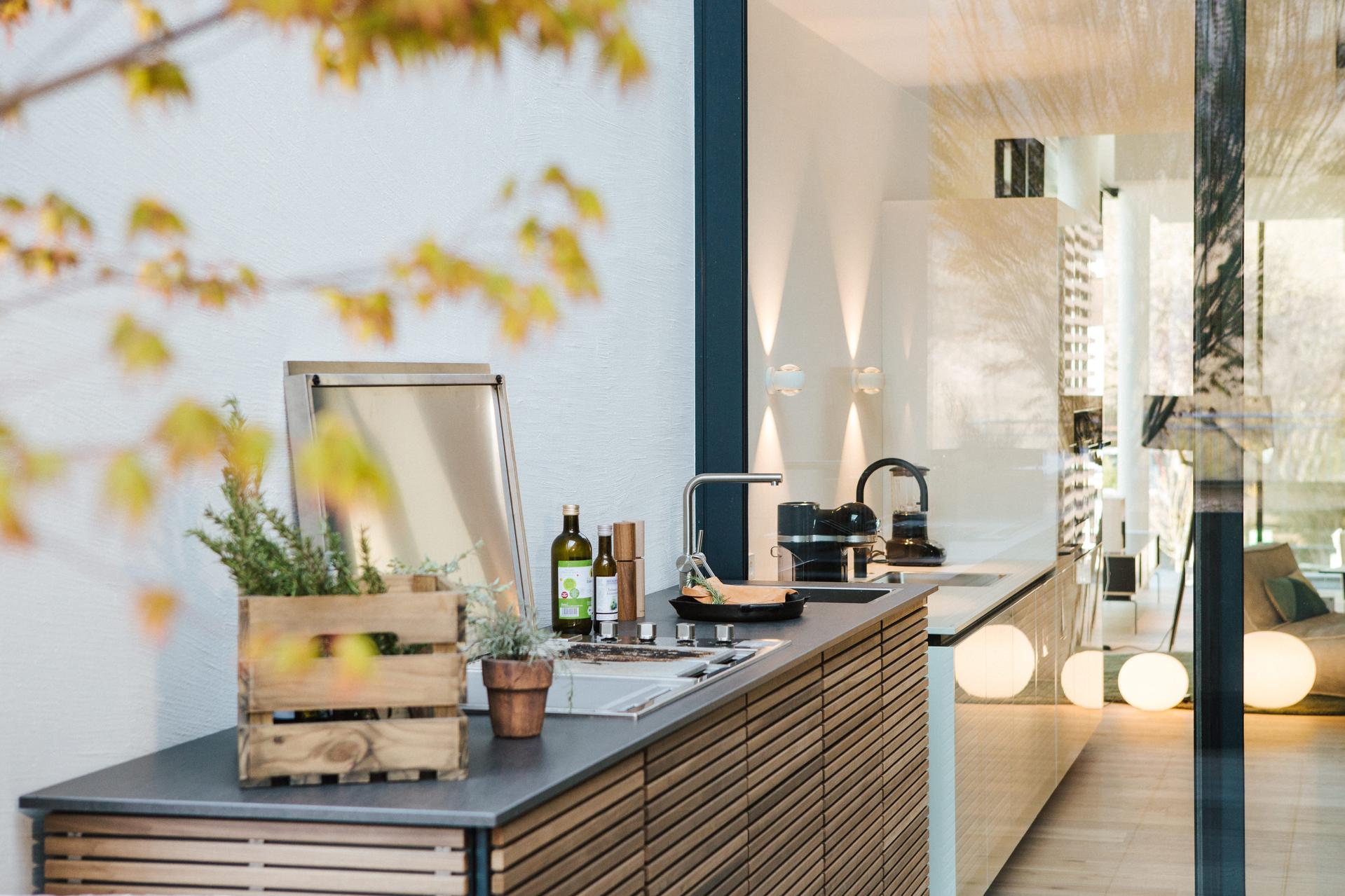 CUBIC-Outdoor-Küche mit Holzlamellen, Kräuterkiste und Spüle auf Terrasse im Herbstlicht