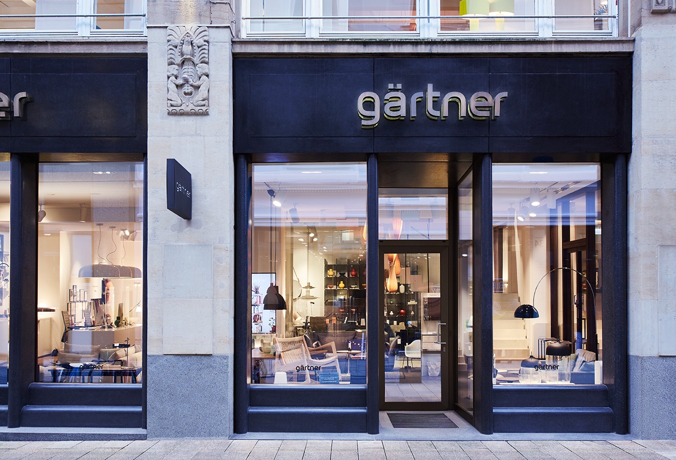 Die Fassade unseres Showrooms in den Großen Bleichen 23 in Hamburg lädt zum Besuch ein. Durch die großen Schaufenster sind verschiedene Designmöbel und Leuchten im Ausstellungsraum zu sehen. Die Treppe führt ins 1. Obergeschoss.