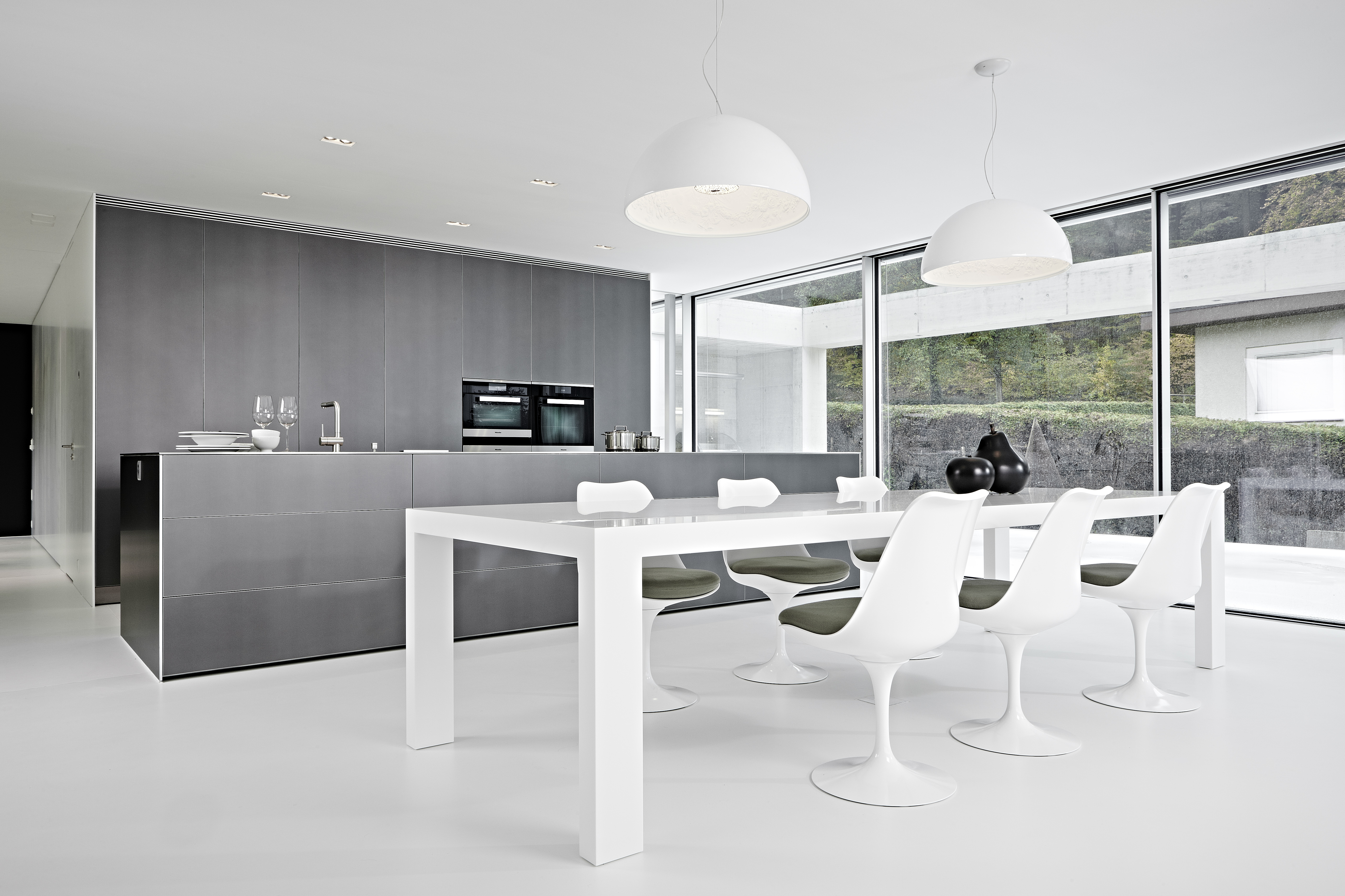 Küche bulthaup b3 und angrenzender Essbereich in Weiß. Tulip Chairs und Esstisch im Tageslicht.   