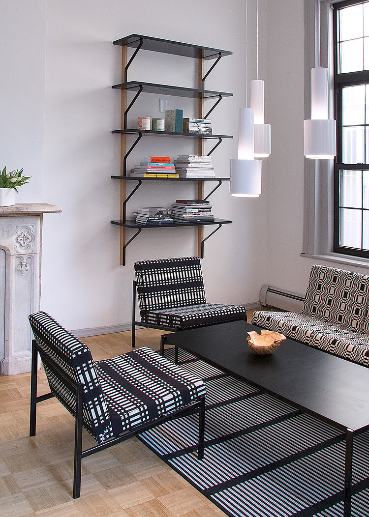 Wohnbereich mit gemusterten Sesseln, schwarzem Tisch und Wandregal mit Büchern