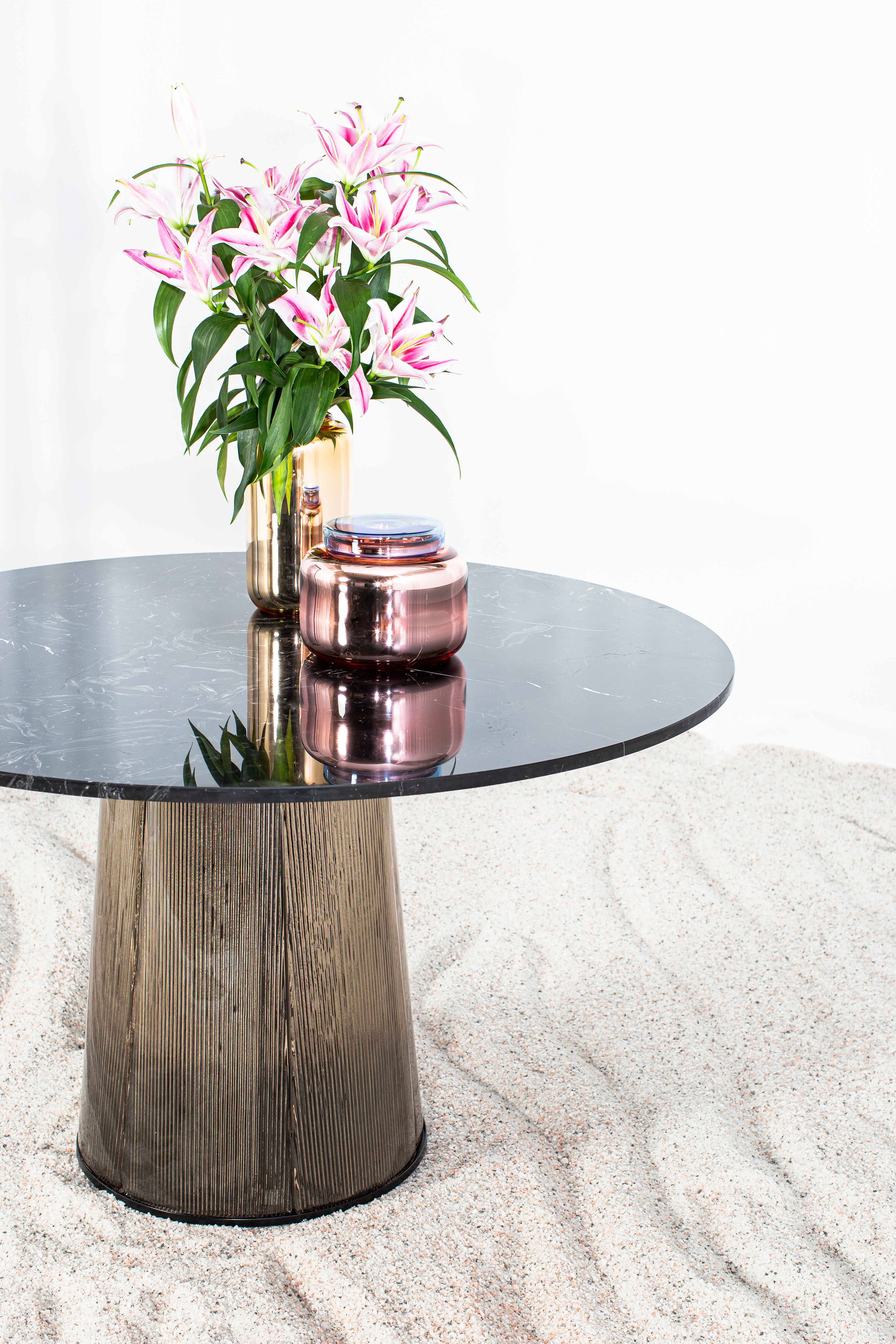 Runder Esstisch mit schwarzer Marmorplatte und Vase auf strukturierter Sandfläche