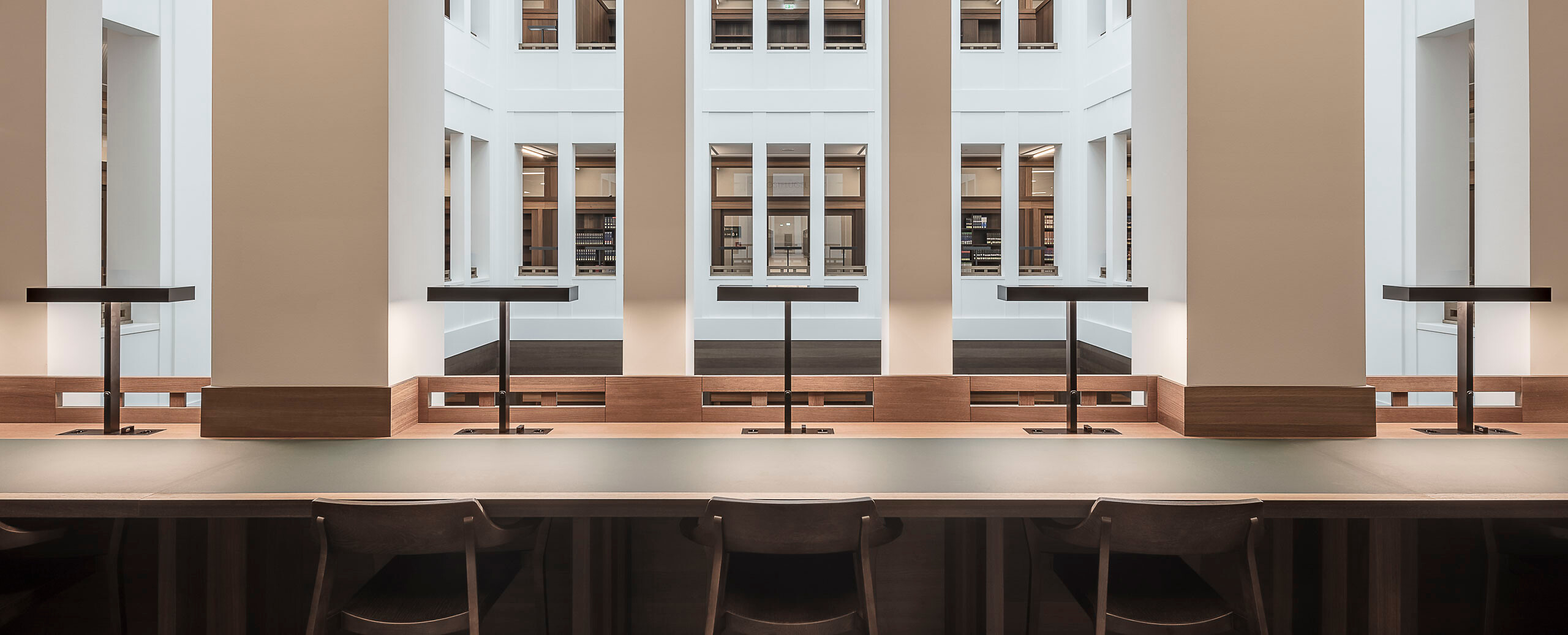 Reihe schwarzer Tischleuchten auf langer Arbeitsfläche im lichten Innenhof einer Bibliothek