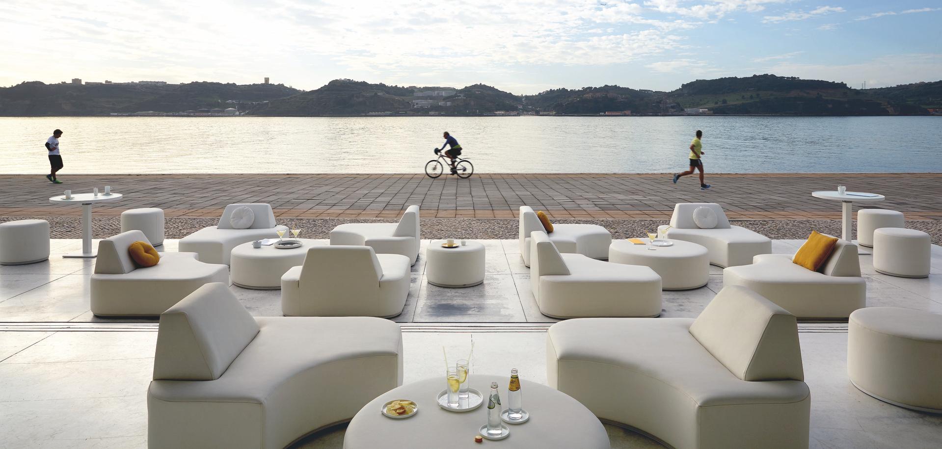 Helle Outdoor-Lounge von Manutti am Wasser, mit runden Modulen und Kissenakzenten