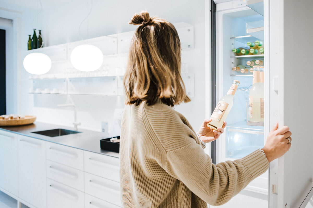 Frau öffnet Kühlschrank in der weißen Teeküche des Café Supernormal und nimmt ein Getränk heraus.