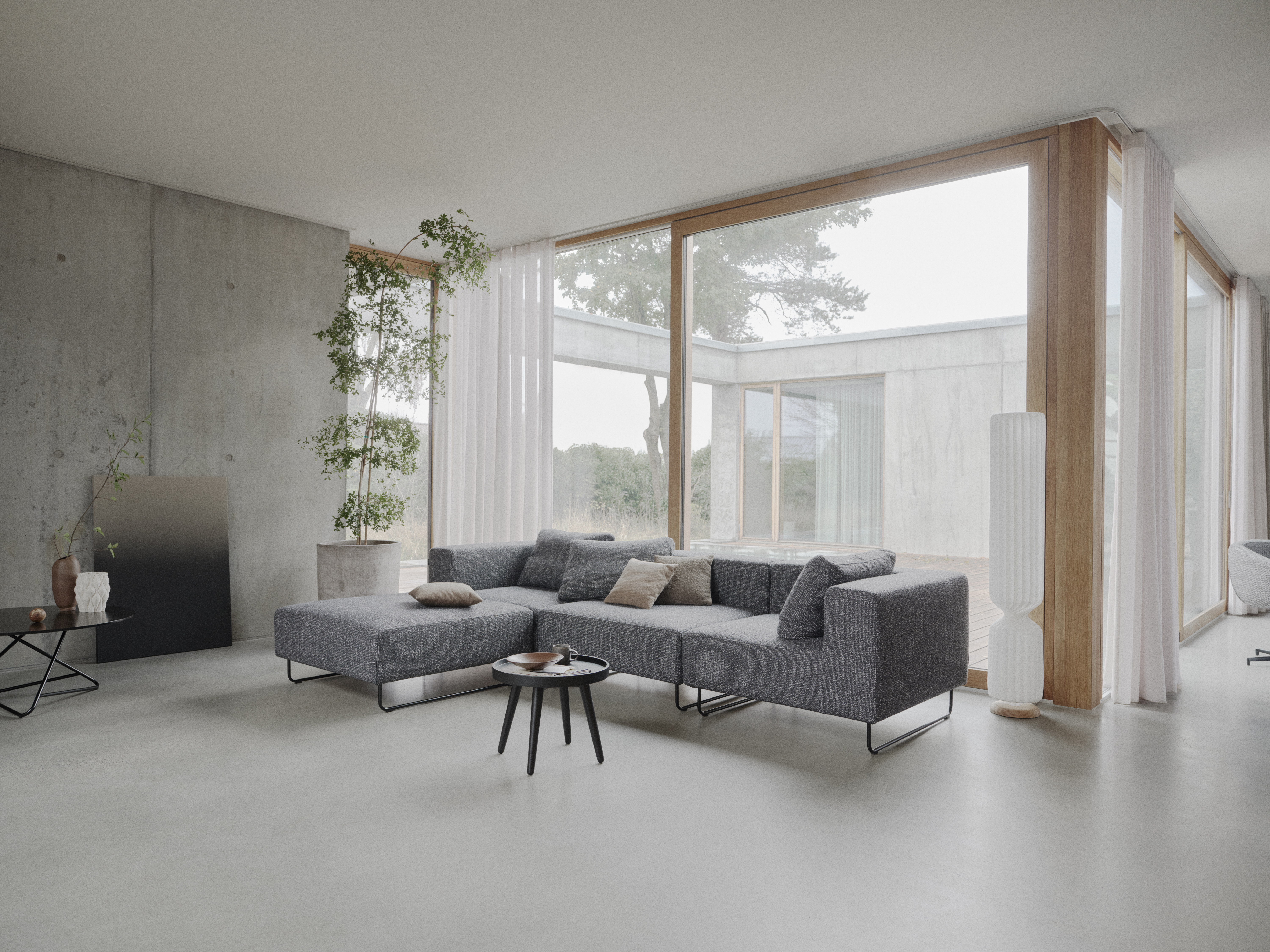 Graues Ecksofa vor bodentiefen Fenstern in einem hellen, puristischen Wohnraum
