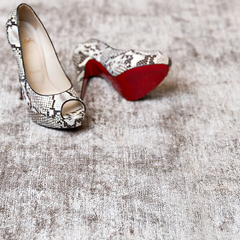 Beiger Teppich mit Pumps in Schlangenoptik mit roter Sohle im Vordergrund
