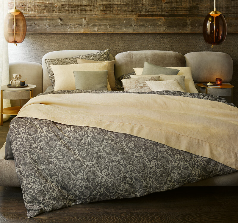 Bett mit dunkler, gemusterter Decke und goldfarbenem Leinenbezug