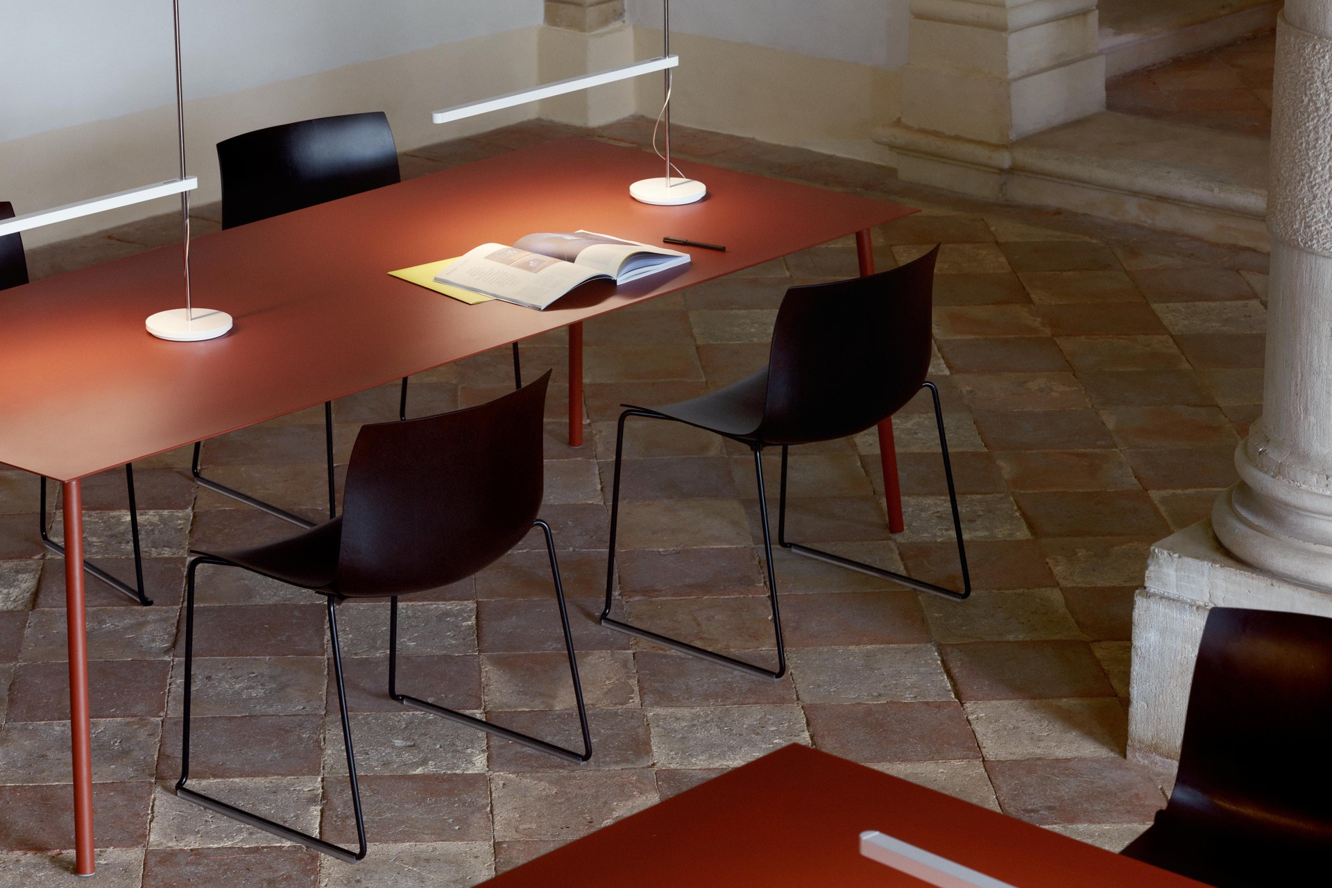 Schlichte Tische mit roter Platte und schwarze Stühle mit Kufengestell in einem Raum mit Steinboden