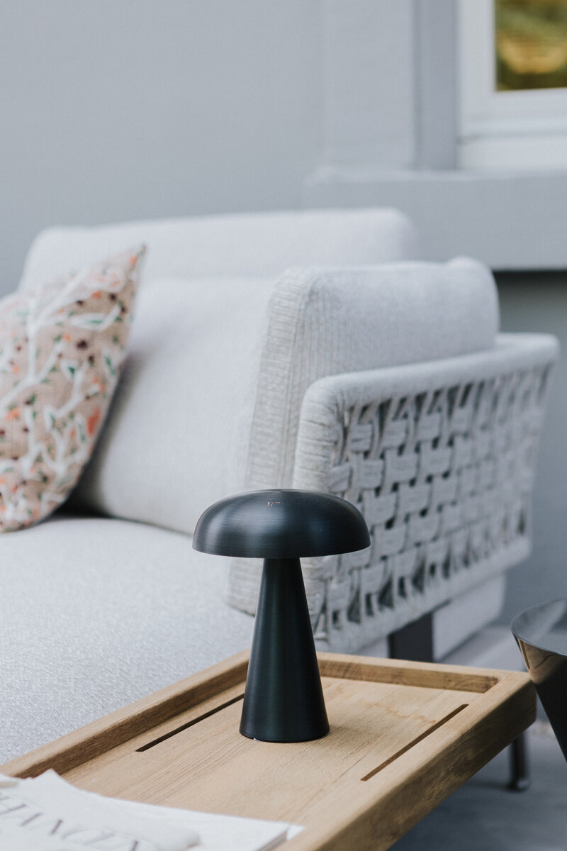 Schwarze Akku-Tischleuchte auf Holztablett vor einem Outdoor-Sessel mit geflochtener Rückenlehne in der Gartenmöbelausstellung in Waldshut bei Seipp Wohnen