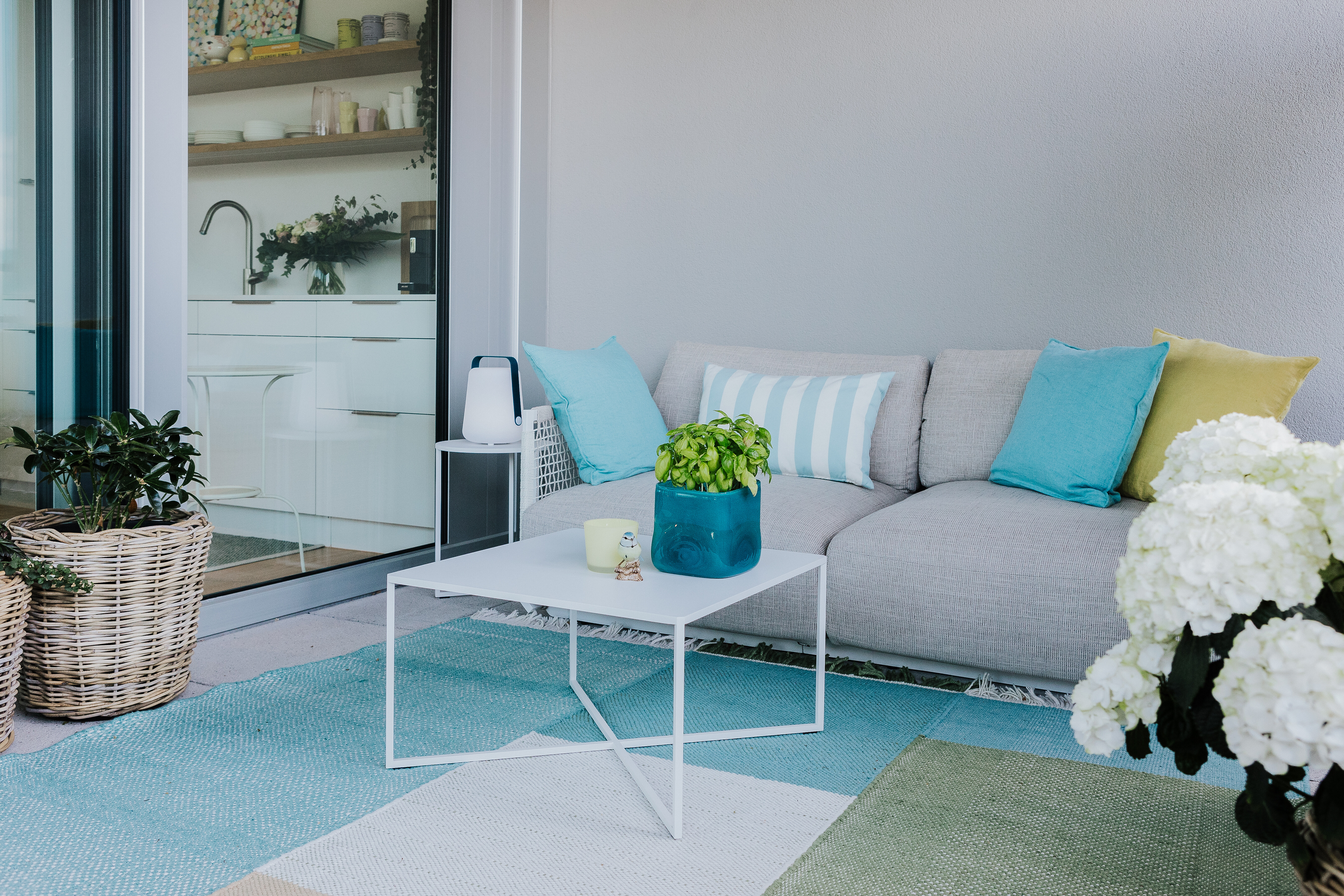 Moderne Terrasse mit Sofa, bunten Kissen, weißem Tisch und Blick auf Innenküche – Seipp Wohnen  