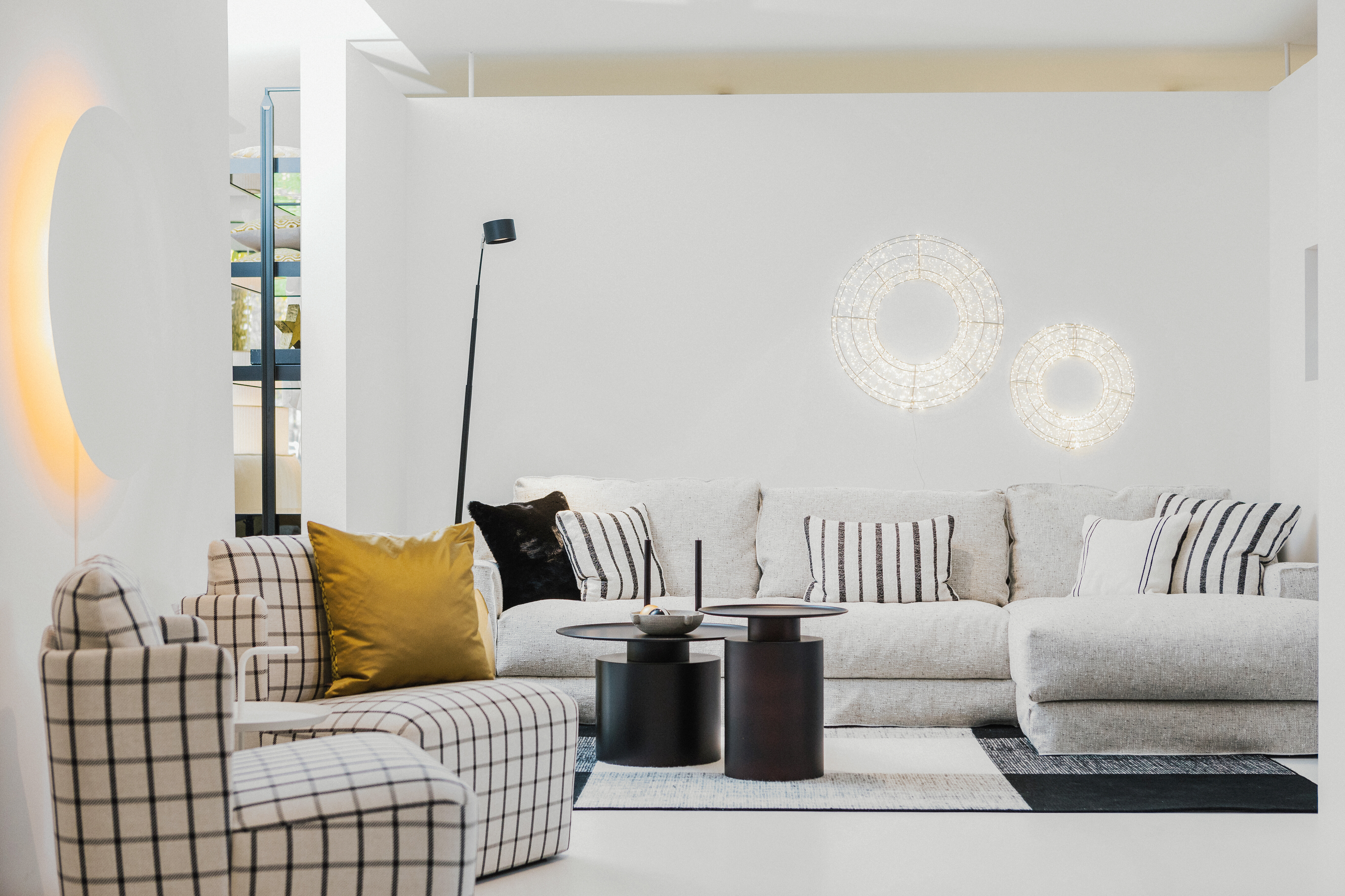 Heller Wohnbereich mit großem Sofa, karierten Sesseln und dekorativer Wandbeleuchtung