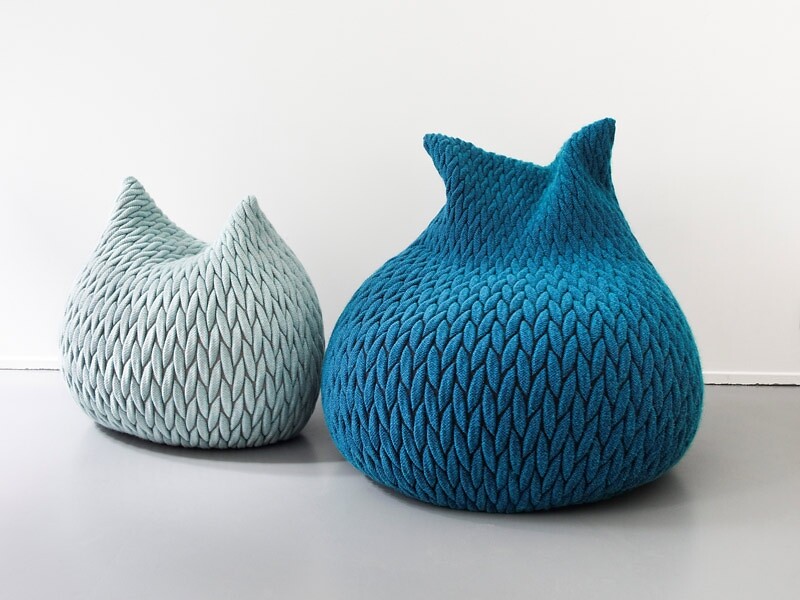 Zwei gestrickte Poufs in Mint und Blau mit spitzer Silhouette vor weißer Wand  