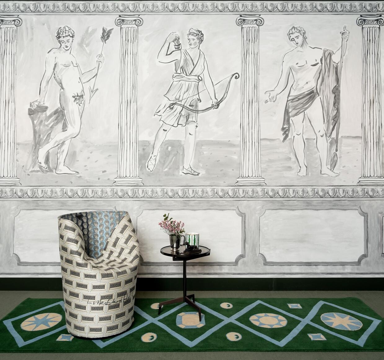 Wand mit antikem Figurenmotiv, grünem Teppich und gemustertem Sessel