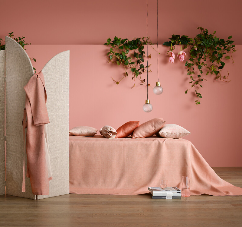 Roséfarbene Bettwäsche mit Kissen vor rosa Wand und hängendem Grün