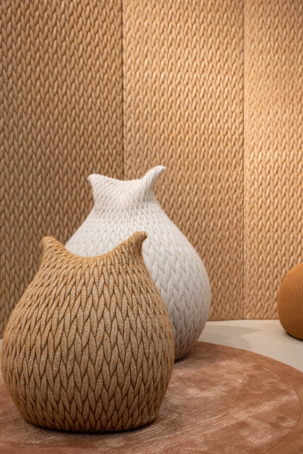 Drei gestrickte Poufs in Beige und Braun auf Teppich vor farblich passender Wand  