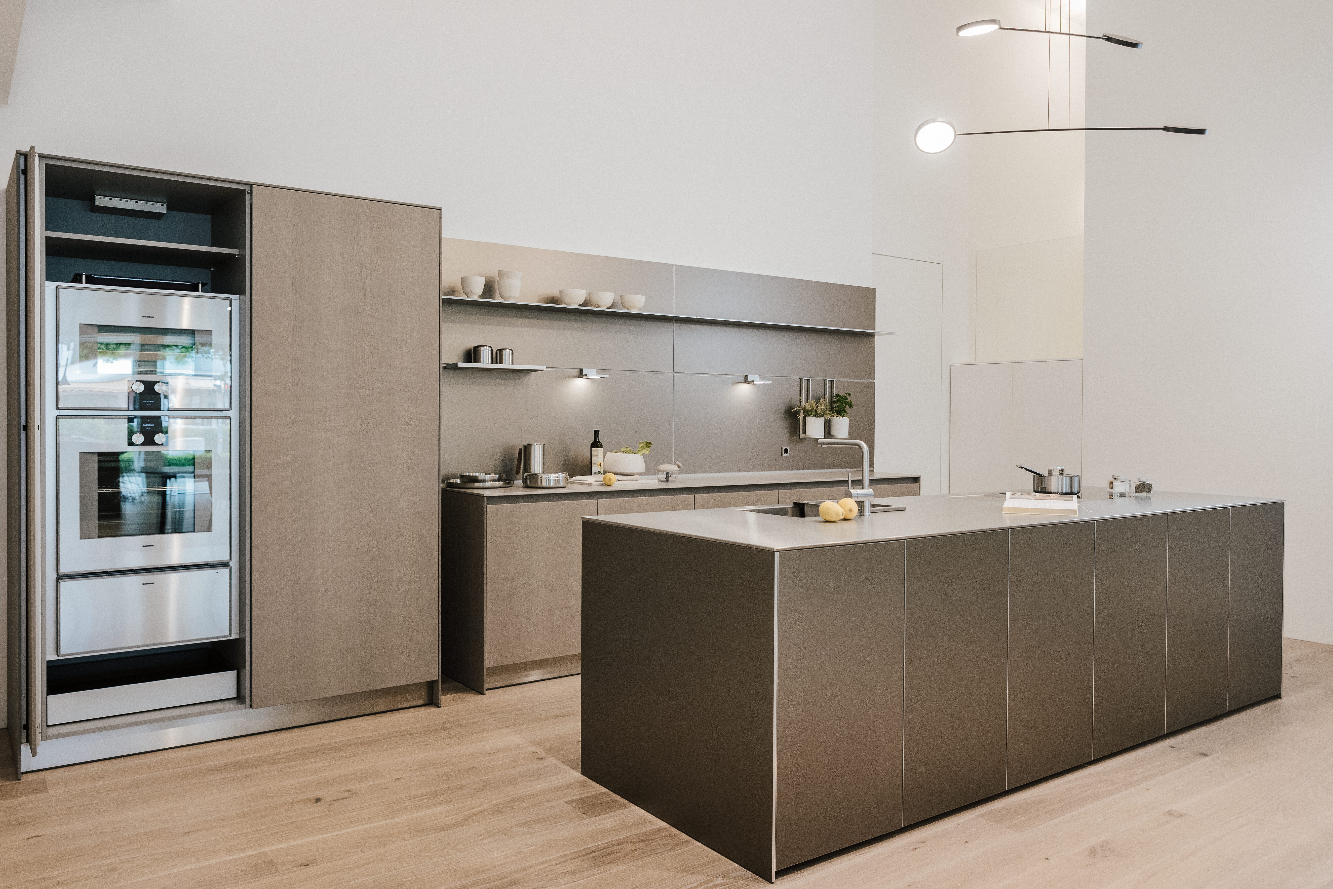 Zeitgemäße Kücheninsel mit grifflosen Fronten in Taupe, Wandzeile mit offenem Regal und Gerätenische