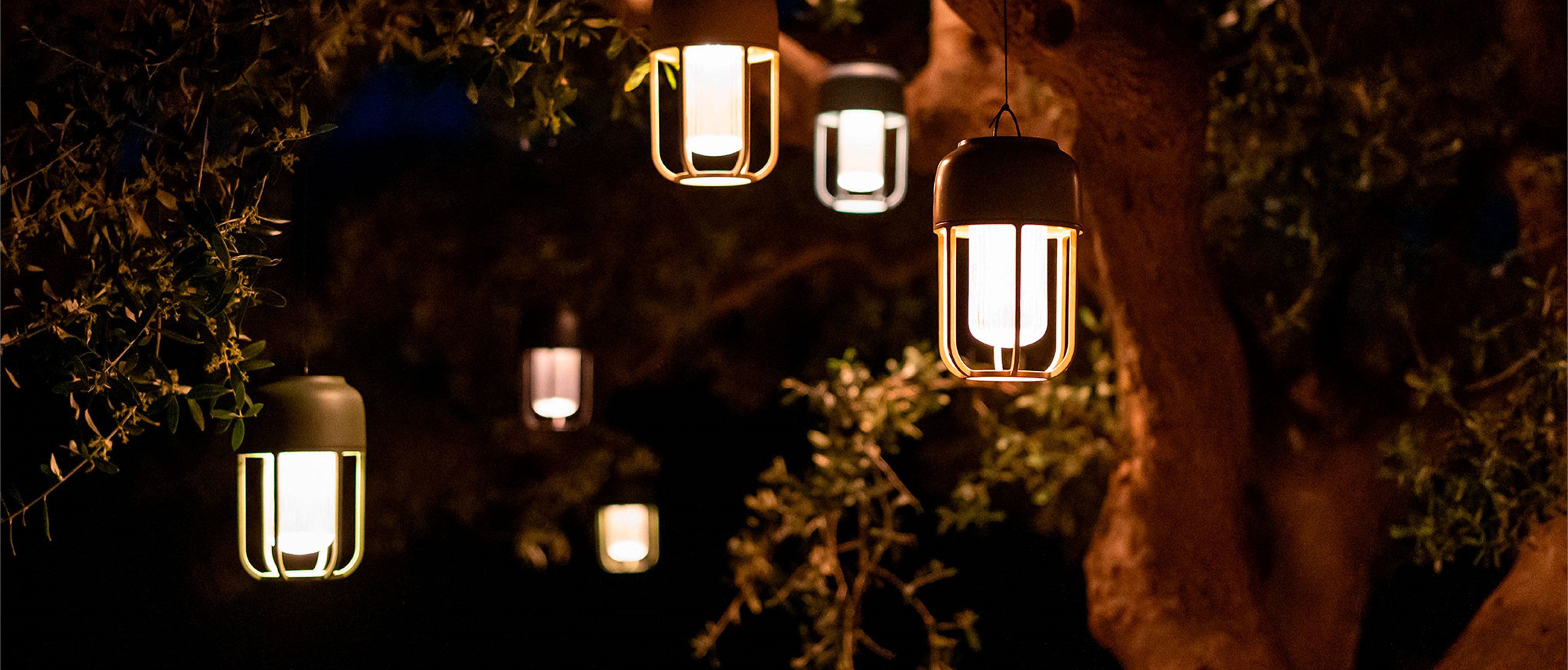 Mehrere Solarleuchten Light No1 von Houe hängen leuchtend in den Ästen eines Baums bei Nacht.