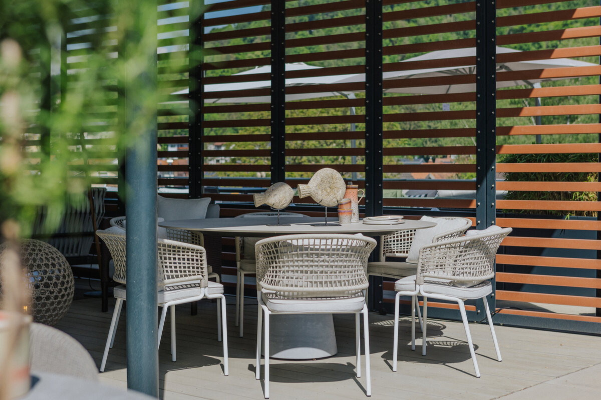 Gartenmöbelausstellung in Tiengen mit rundem Tisch und hellen Flechtstühlen vor moderner Holzverschattung  