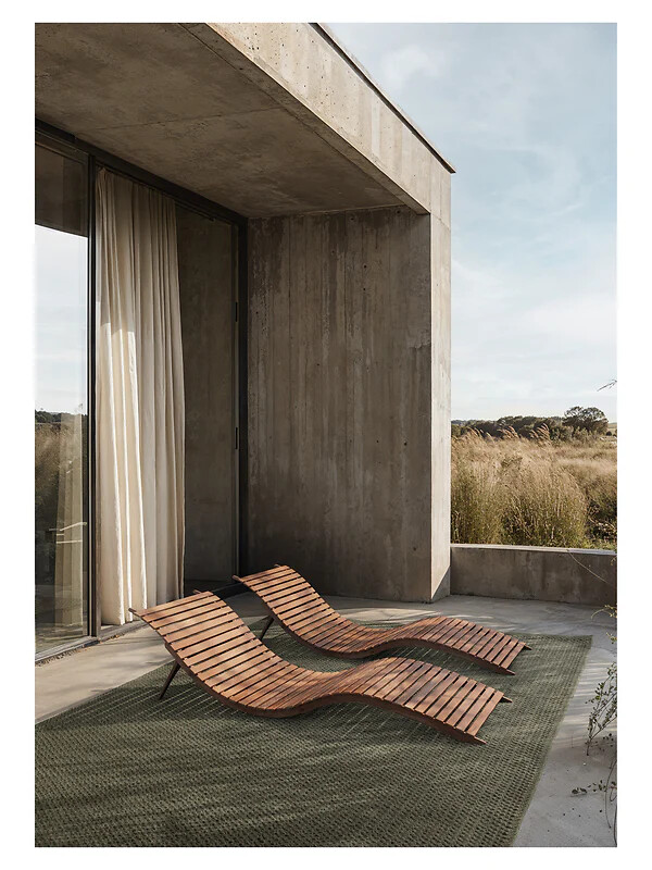 Grüner Outdoorteppich unter Holzliegen vor Betonwand und Gräsern