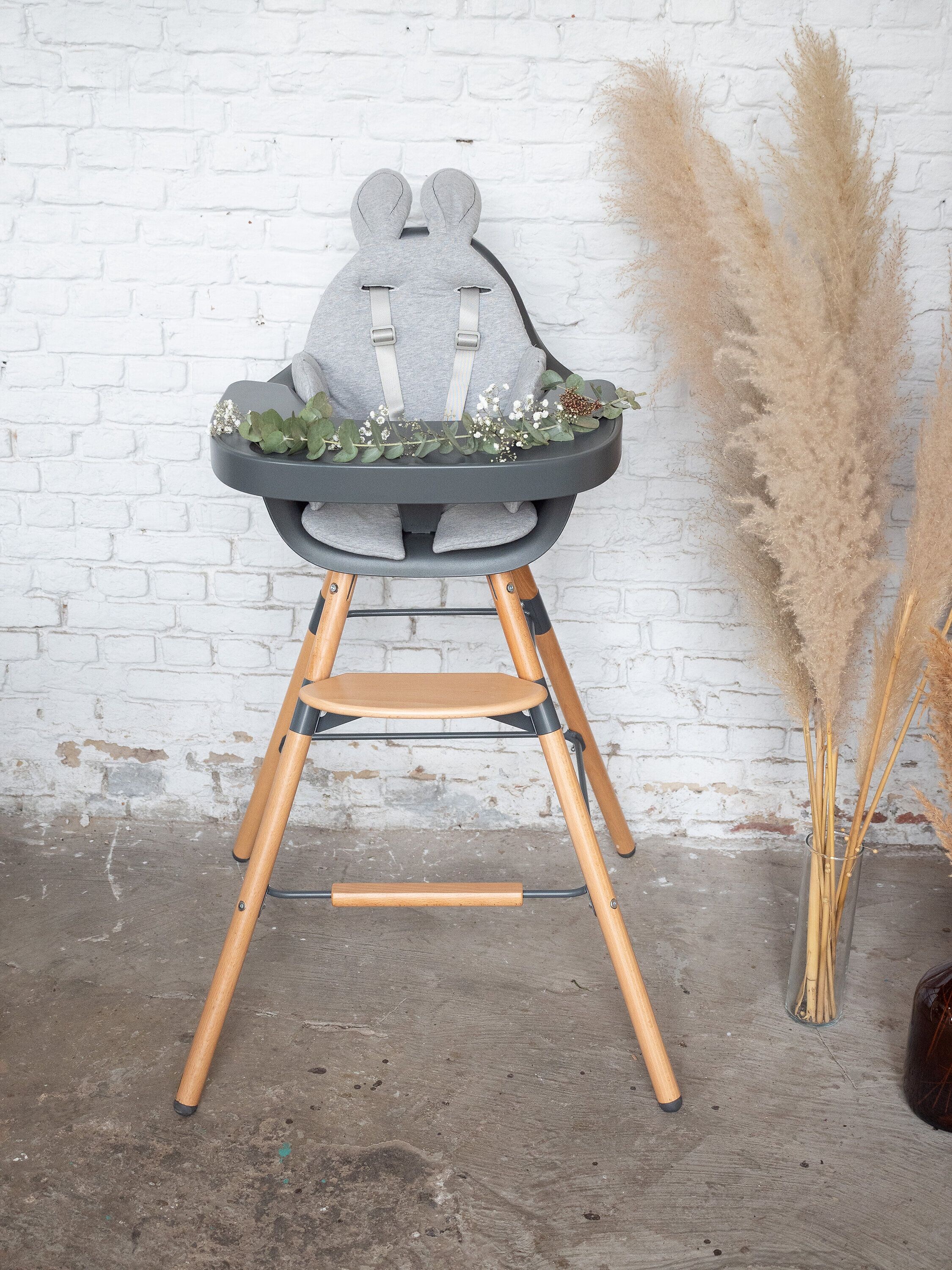 Grauer Hochstuhl mit Holzbeinen, gepolstertem Gurtsystem und Hasenohren-Sitzverkleinerer