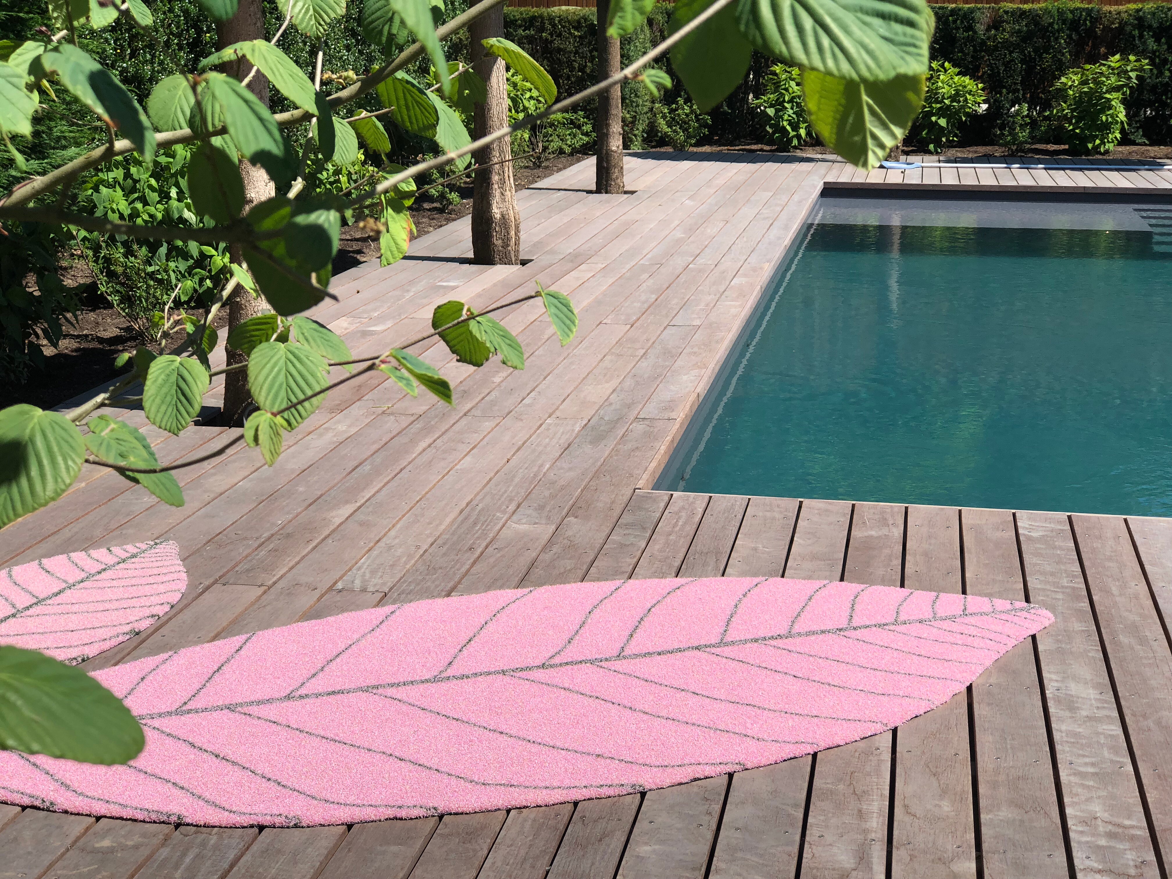 Pooldeck mit pinkfarbenem Teppich in Form eines stilisierten Blattes, umgeben von Holzplanken  
