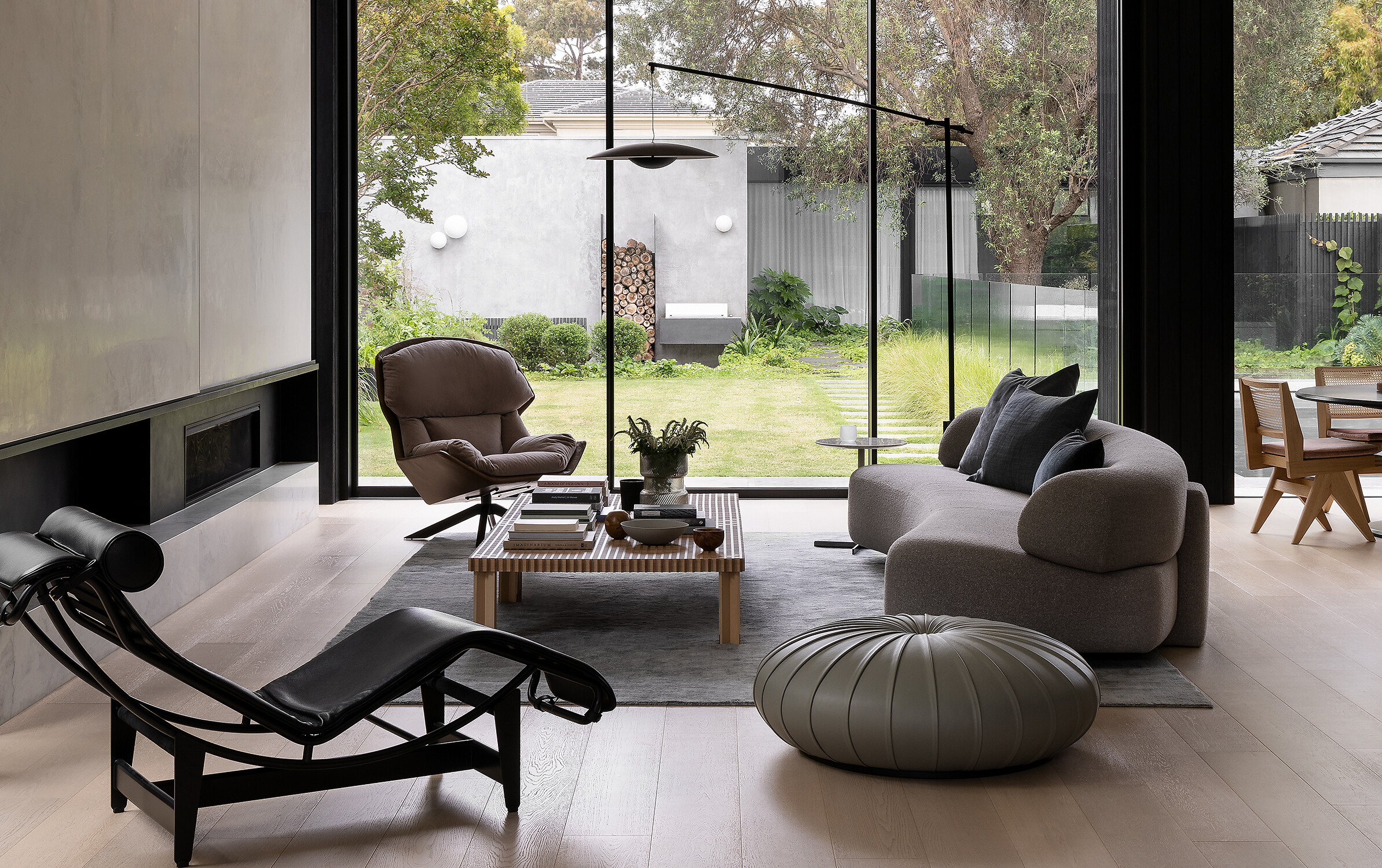 Wohnzimmer mit Sessel, gepolertem Sofa, Lederliege und Pouf vor bodentiefer Verglasung