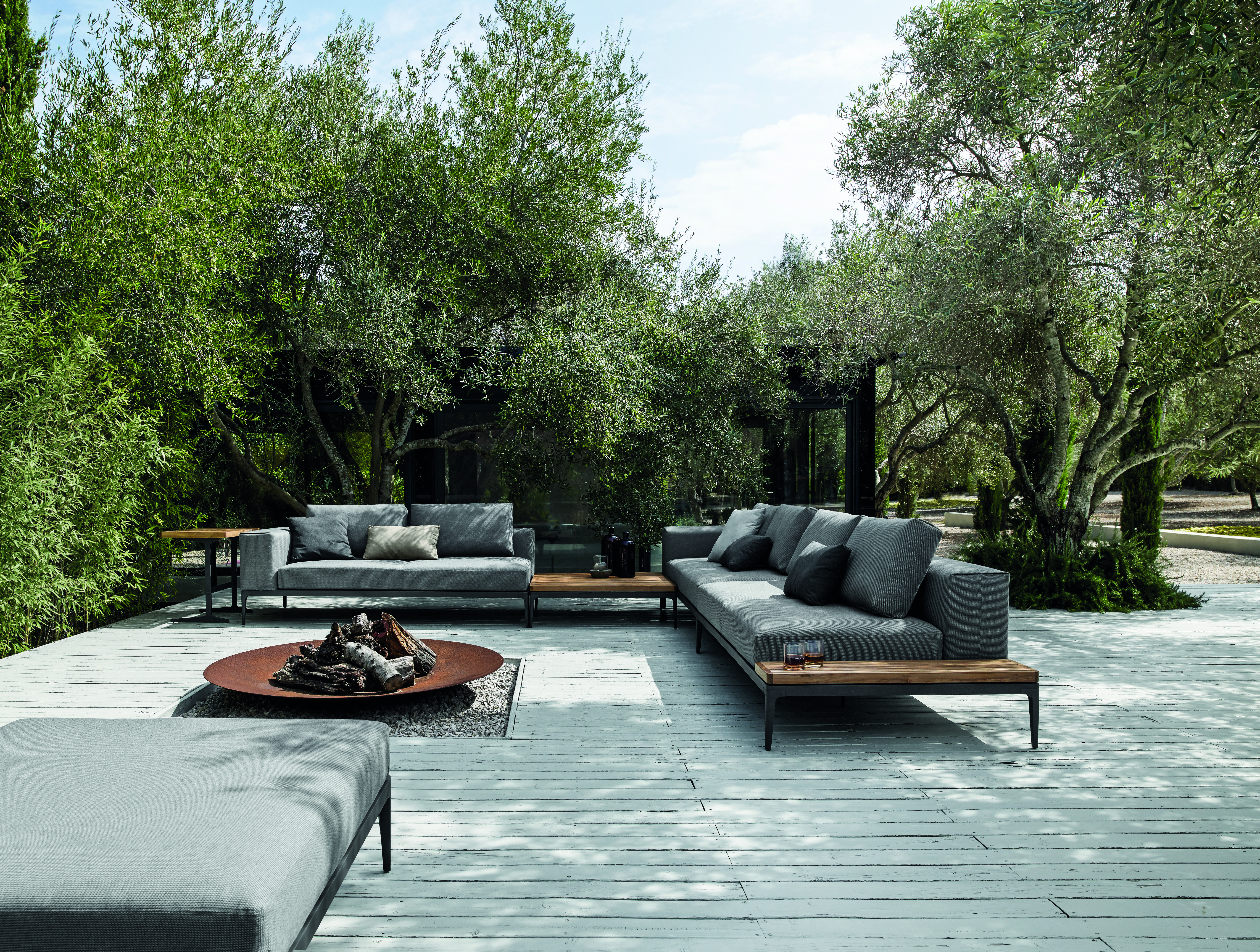 Zwei Outdoor-Sofas mit Holzablage auf heller Terrasse, umgeben von Olivenbäumen