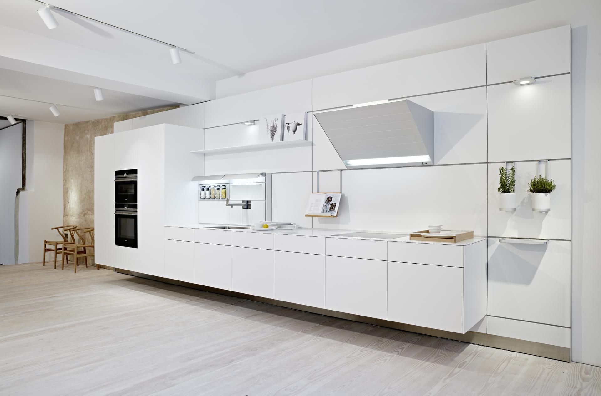 Bulthaup Küche mit wandhängenden, grifflosen Fronten in Weiß und markanter, integrierter Dunstabzug
