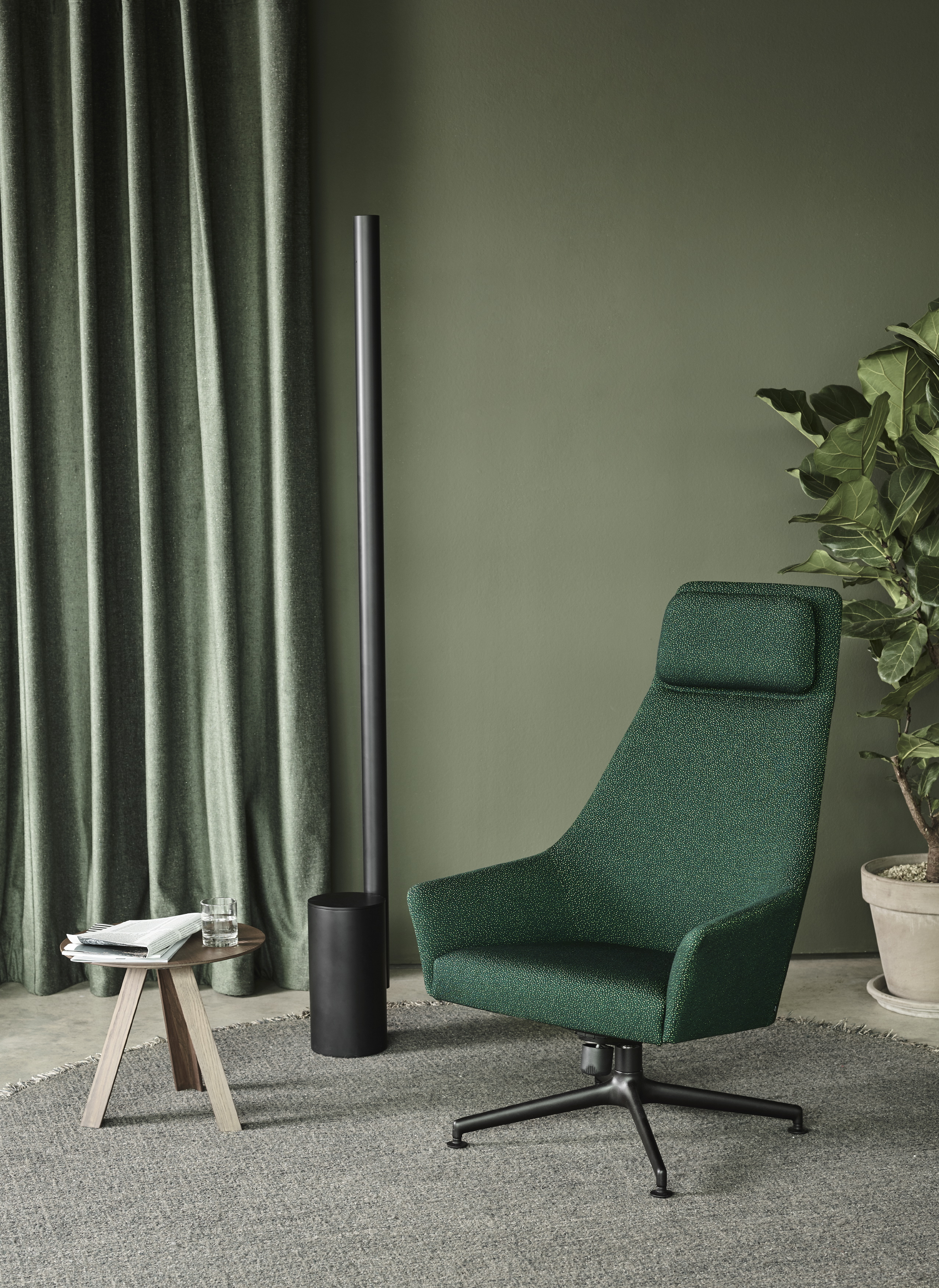 Hoher Polstersessel in grünem Stoff auf schwarzem Drehgestell vor grüner Wand