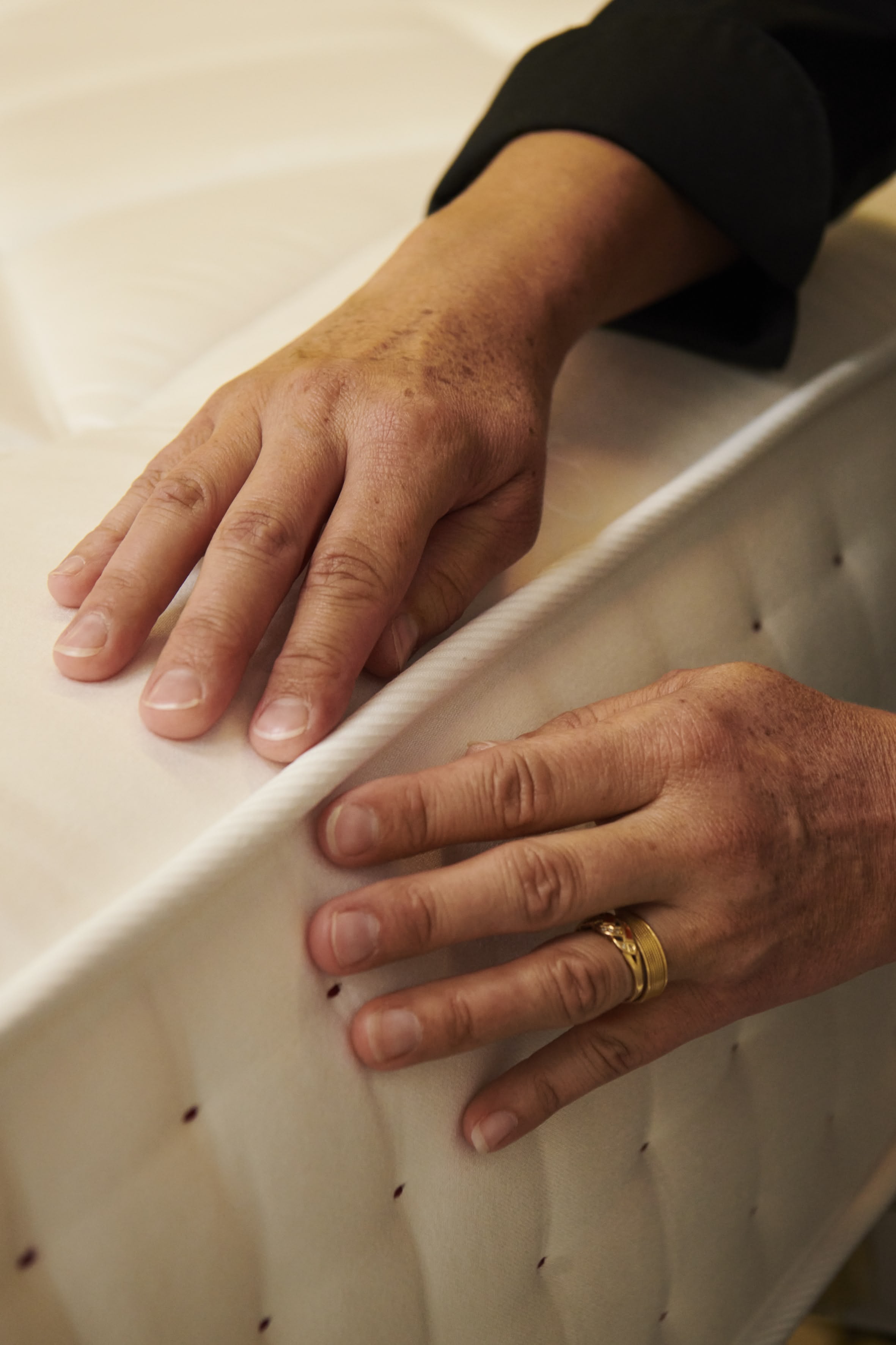 Zwei Hände prüfen die Oberfläche einer Matratze mit abgestepptem Bezug in handwerklicher Qualität