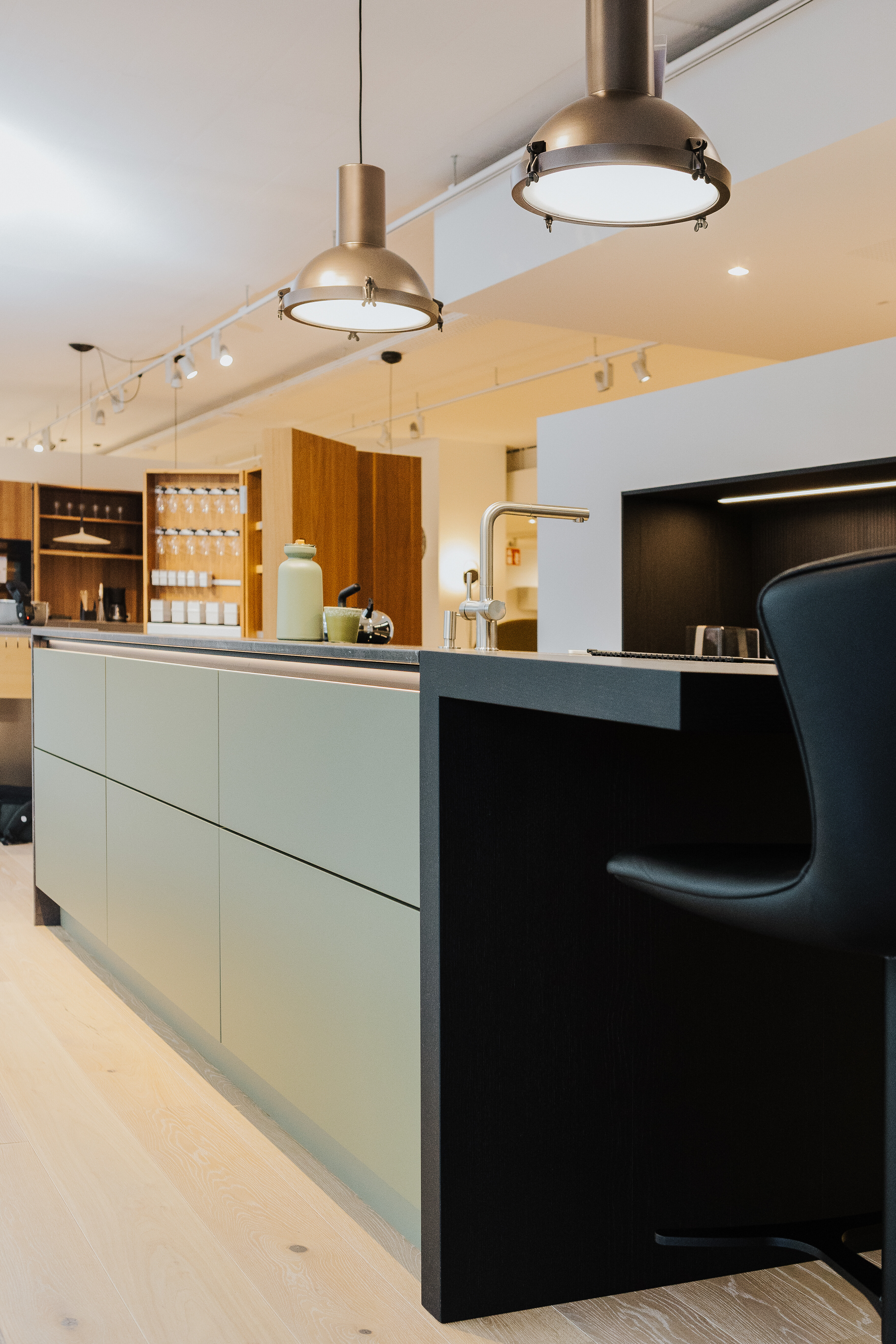 Küchenausstellung mit grünlich-grauer Nolte Inselküche und markanten Hängelampen