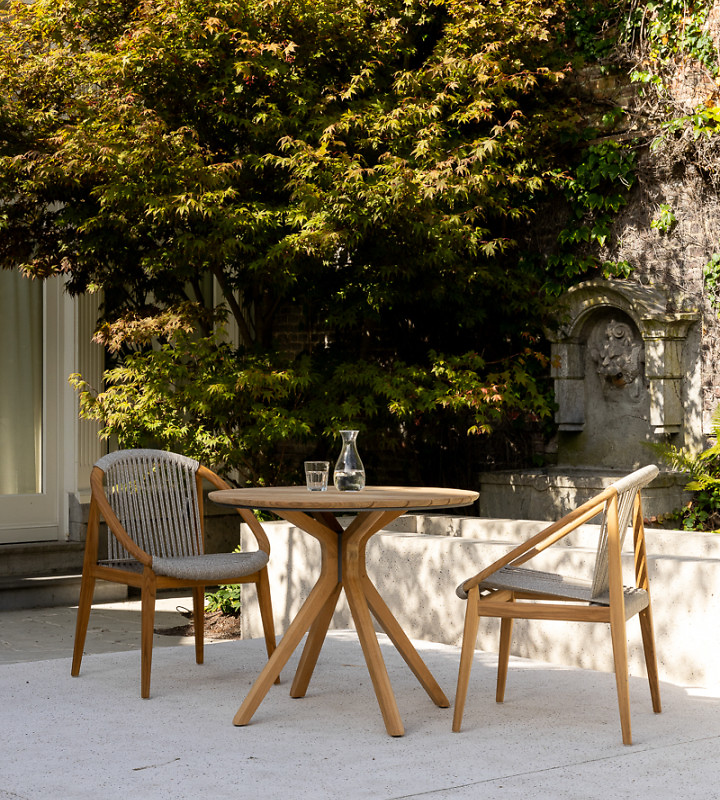 Zwei Stühle mit Rundlehne und runder Tisch aus Holz auf heller Terrasse im Garten