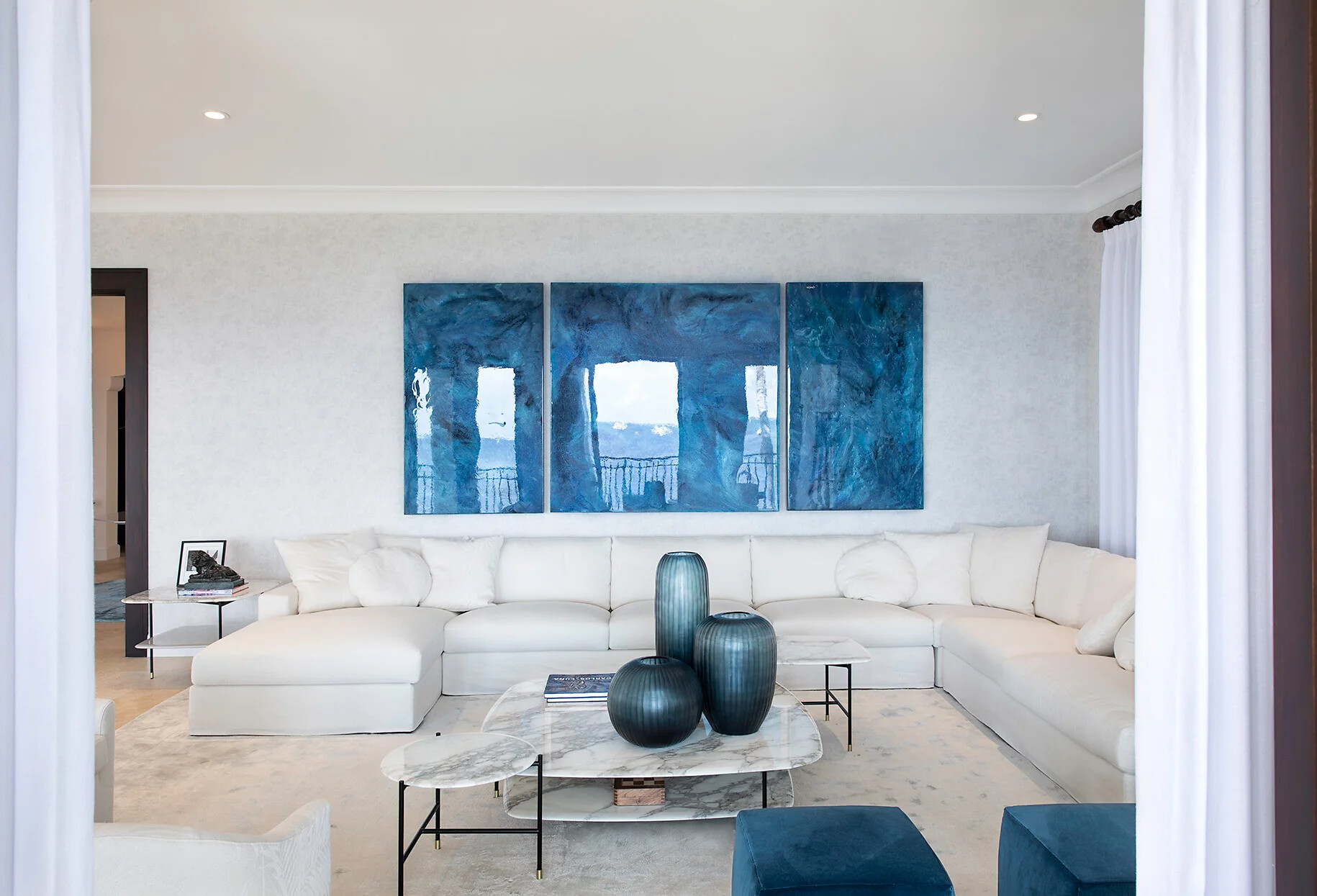 Wohnraum mit weißem Sofa und drei großformatigen blauen Kunstwerken an der Wand  