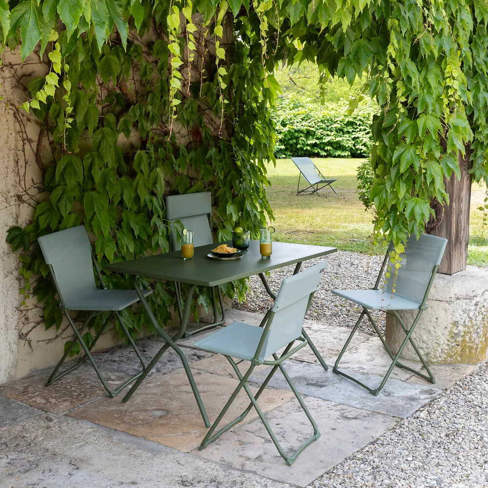 Klappbare Gartenmöbel in Salbeigrün unter mit Wein bewachsener Pergola auf Natursteinboden