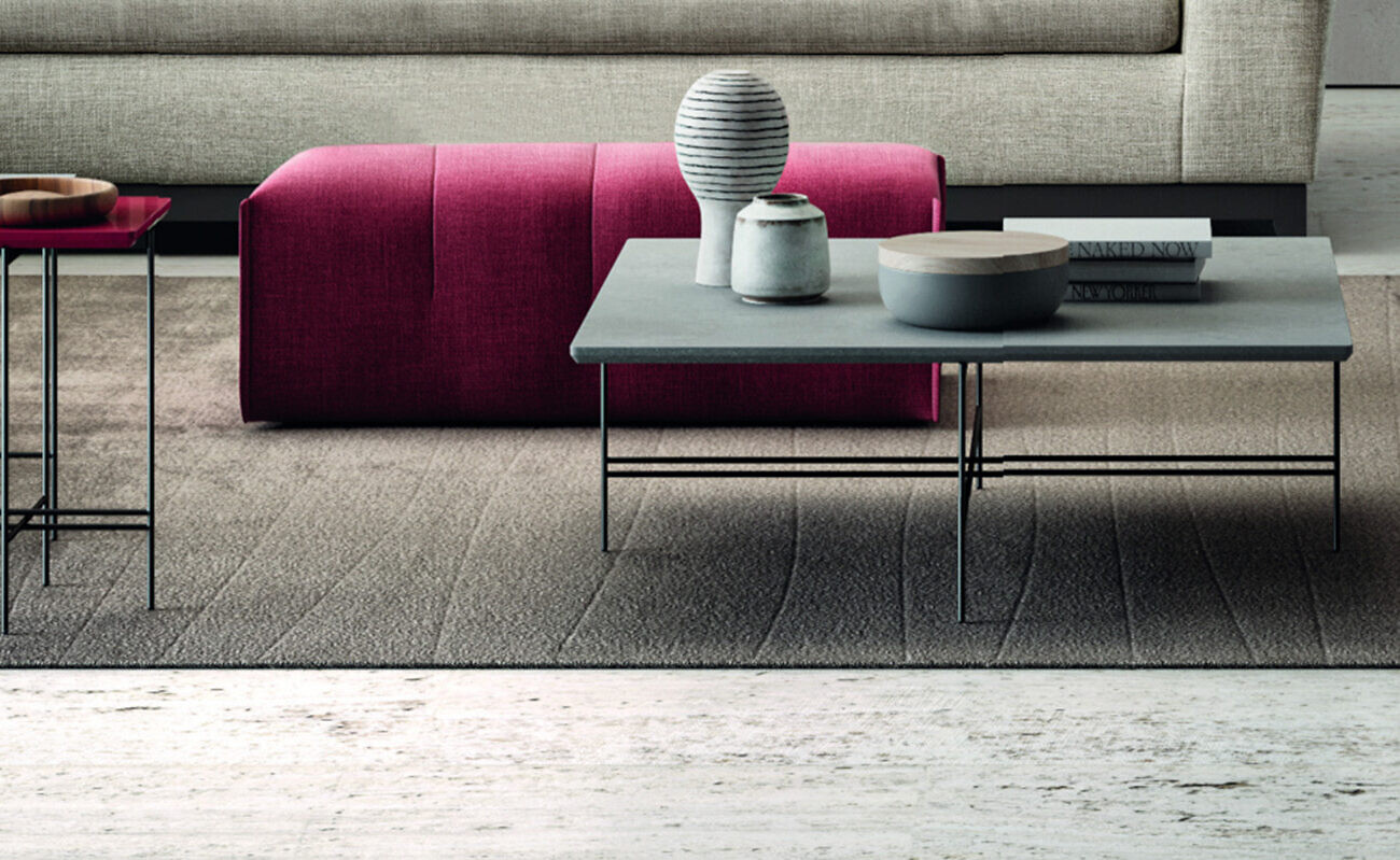 Magentafarbener Pouf kombiniert mit grauem Couchtisch und Accessoires auf Teppichboden  