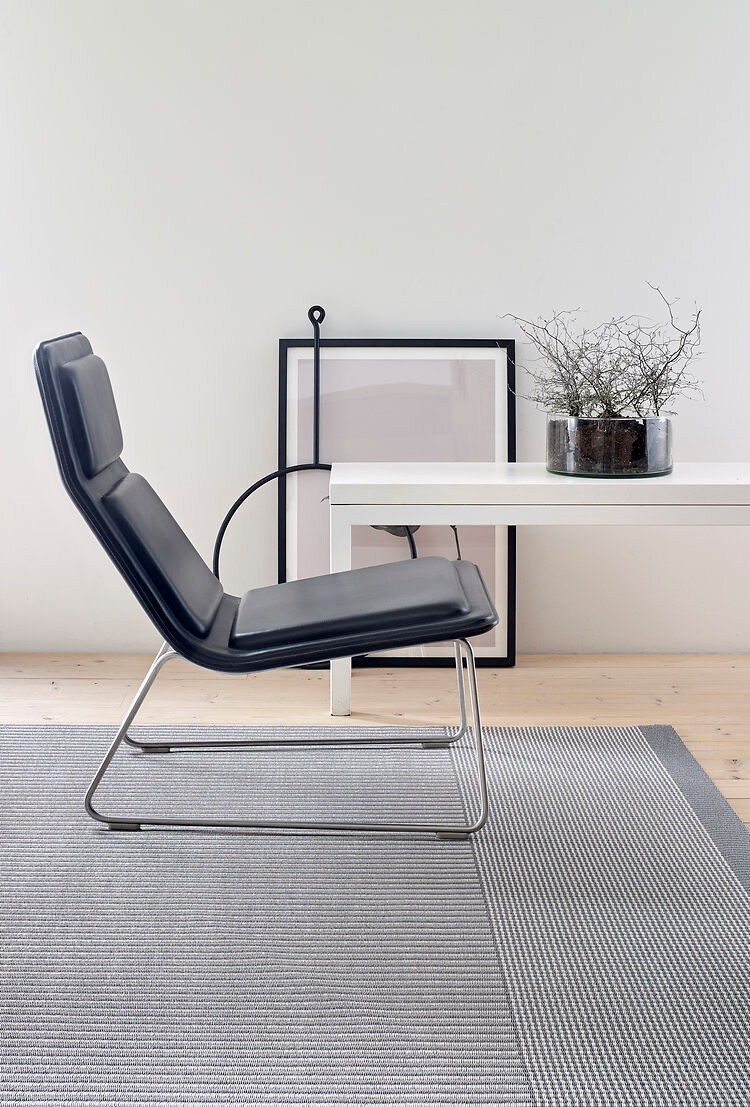 Moderner Sessel in Schwarz auf hellgrauem Teppich mit geometrischer Webstruktur