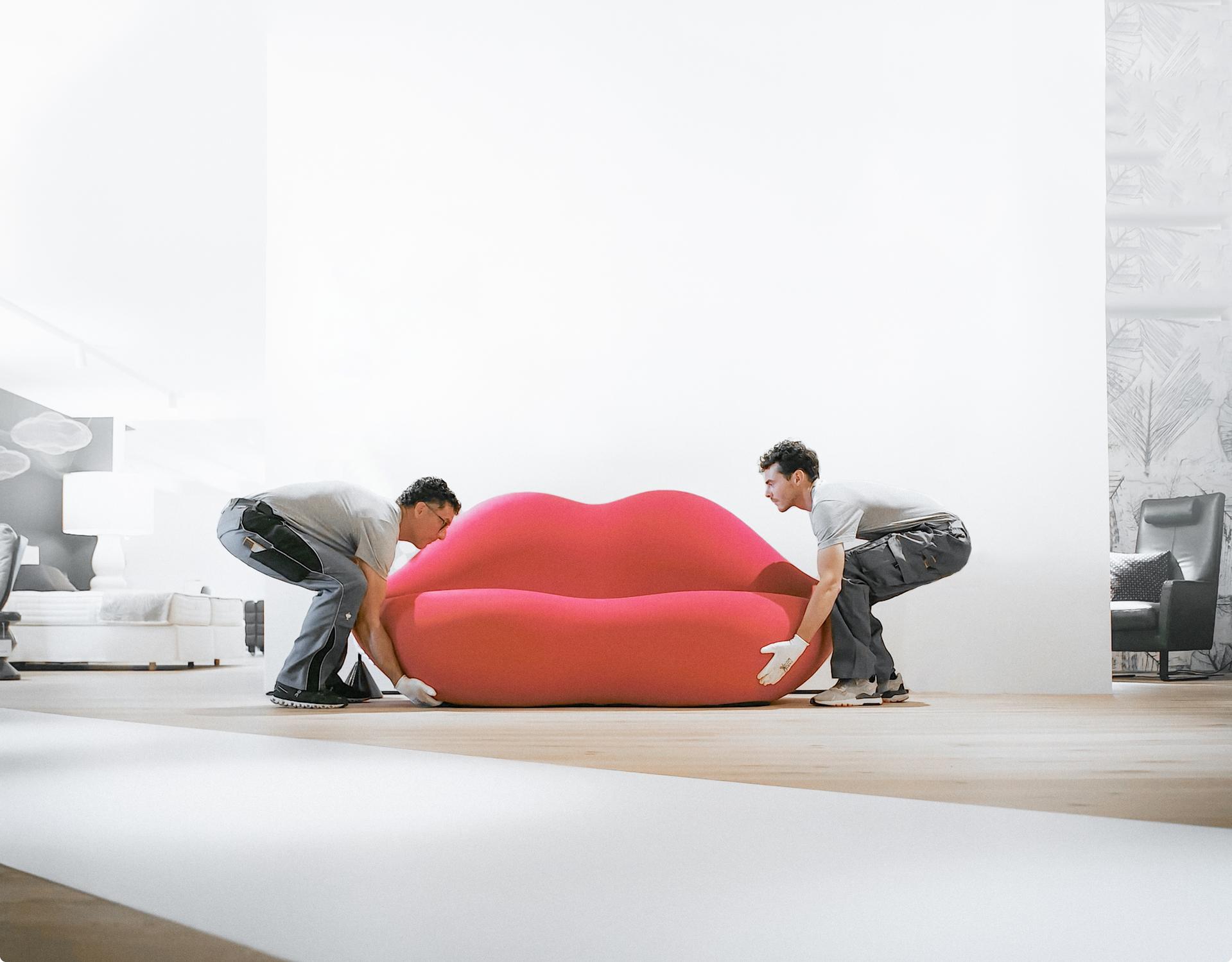 Zwei Monteure von Seipp Wohnen platzieren ein knallrotes Bocca-Sofa in einer hellen Ausstellungsfläche.